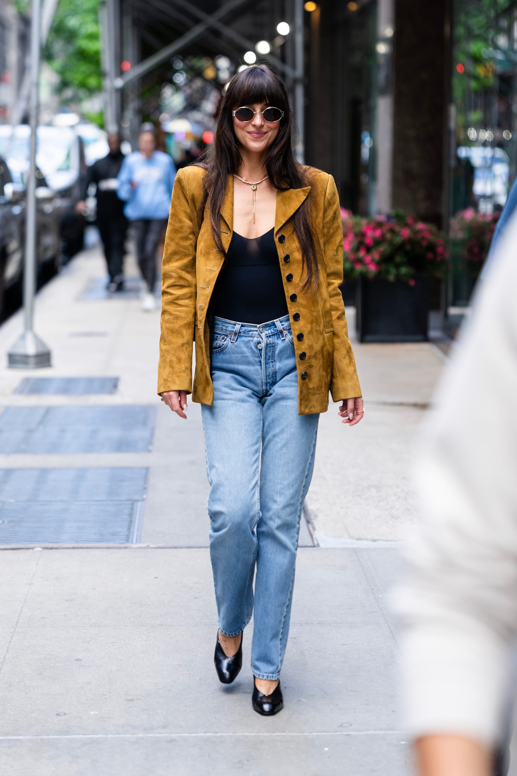 Dakota Johnson walks through New York City while wearing jeans and a yellow jacket.