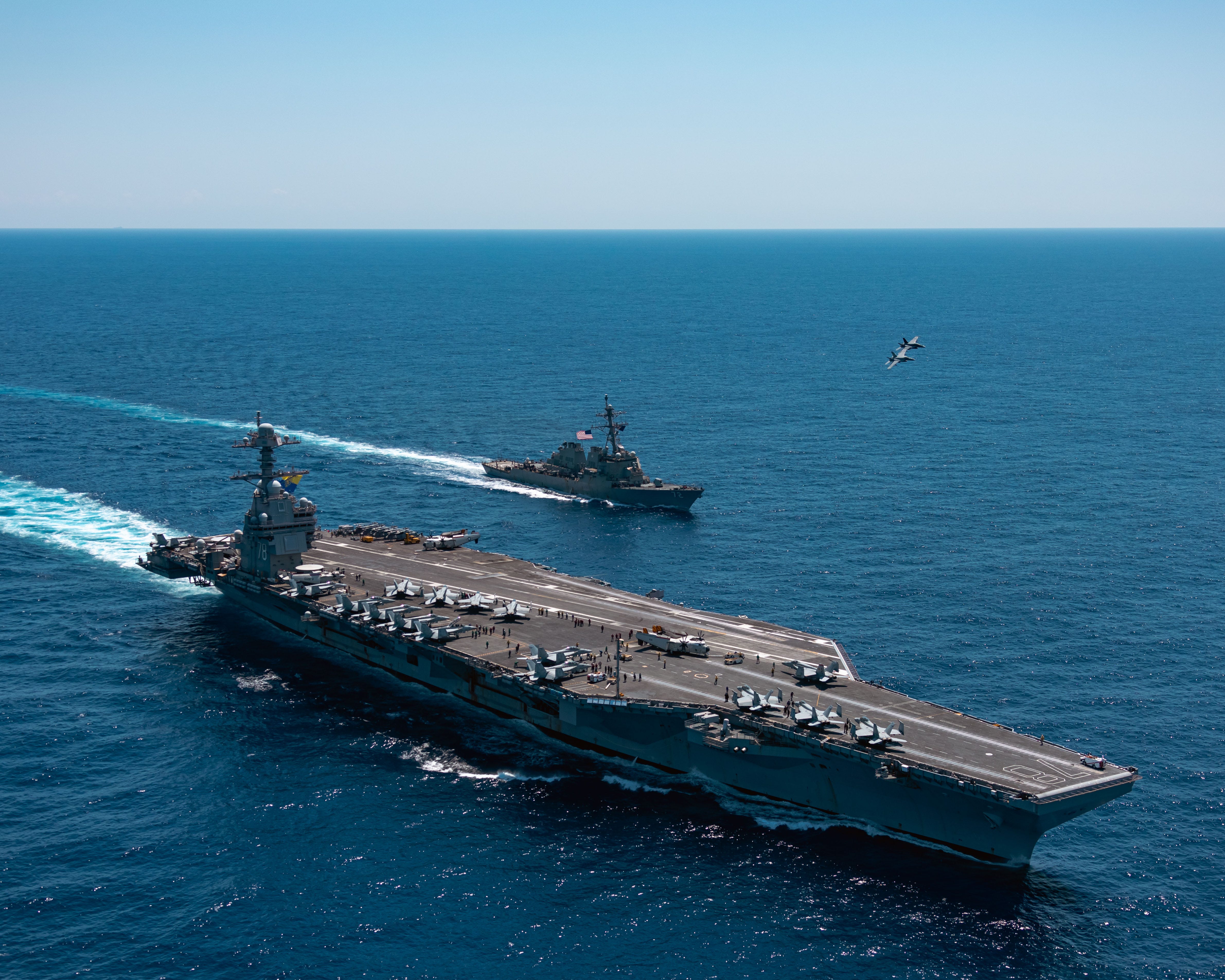 An F/A-18F Super Hornet, attached to the "Blacklions" of Strike Fighter Squadron (VFA) 213, and a F/A-18E Super Hornet, attached to the "Golden Warriors" of Strike Fighter Squadron (VFA) 87, fly over USS Gerald R. Ford and the Arleigh Burke-class guided-missile destroyer USS Mahan.