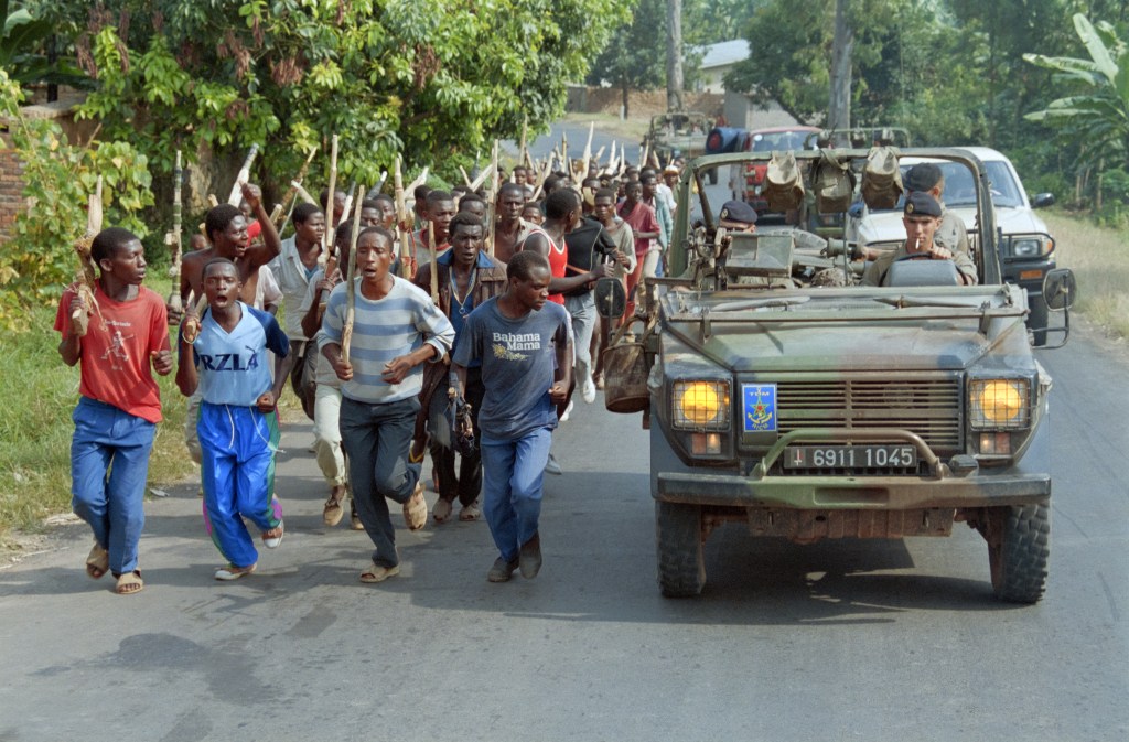 French soldiers of the marine tank infantry regiment participating in the French-led military Operation Turquoise, patrol and pass Hutu troops from the Rwandan government forces training with sticks, on June 27, 1994.