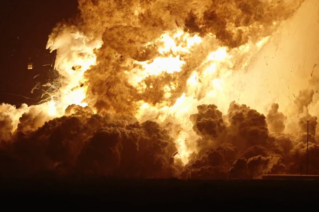 Debris is scattered around the test site as flames shoot up into the air.