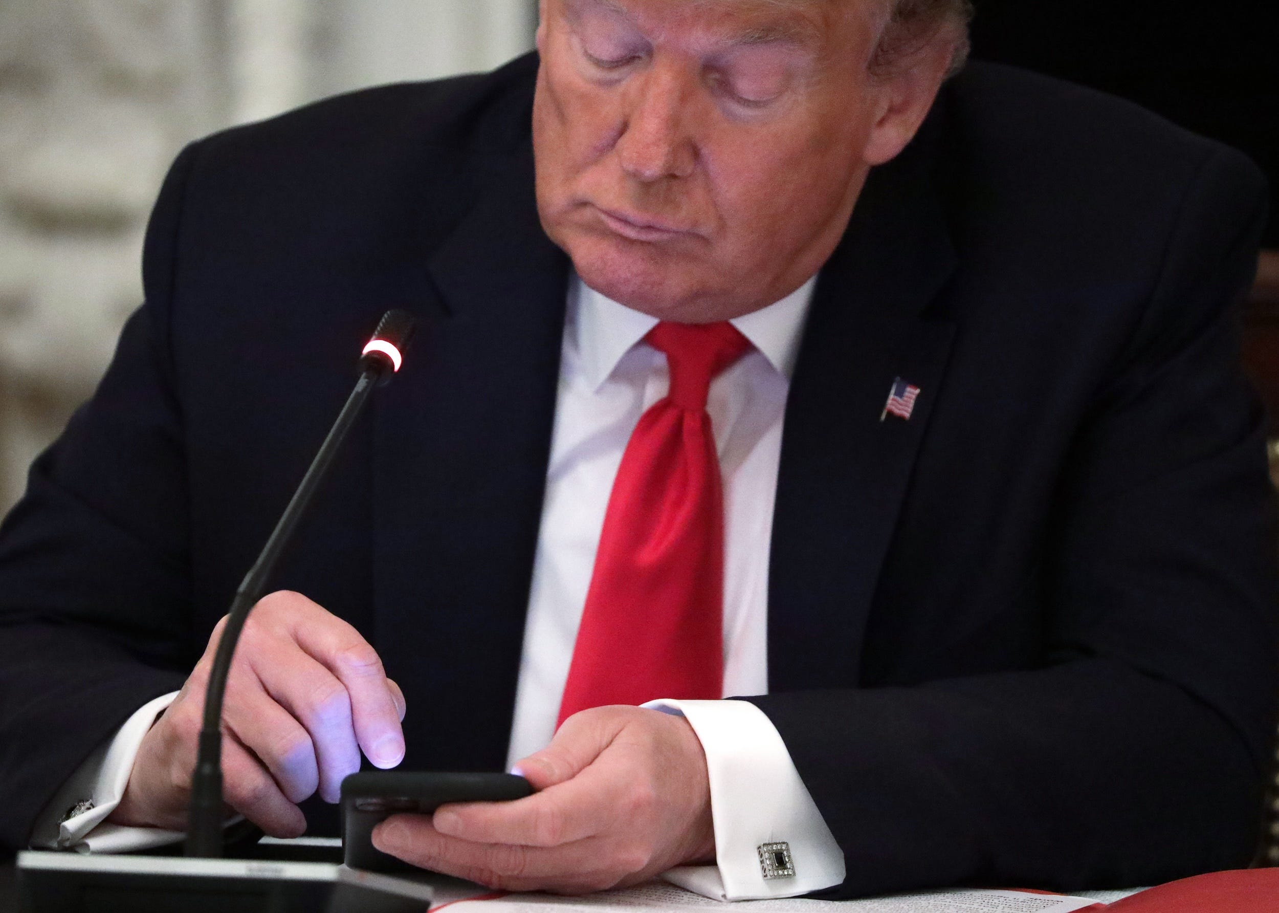 Trump looks down at his phone during a 2020 roundtable meeting at the White House
