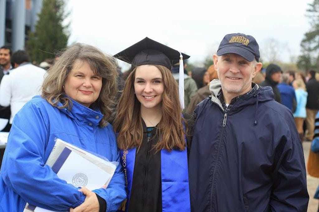 The author with her parents at graduation, wearing a cap and gown, standing between them and smiling.
