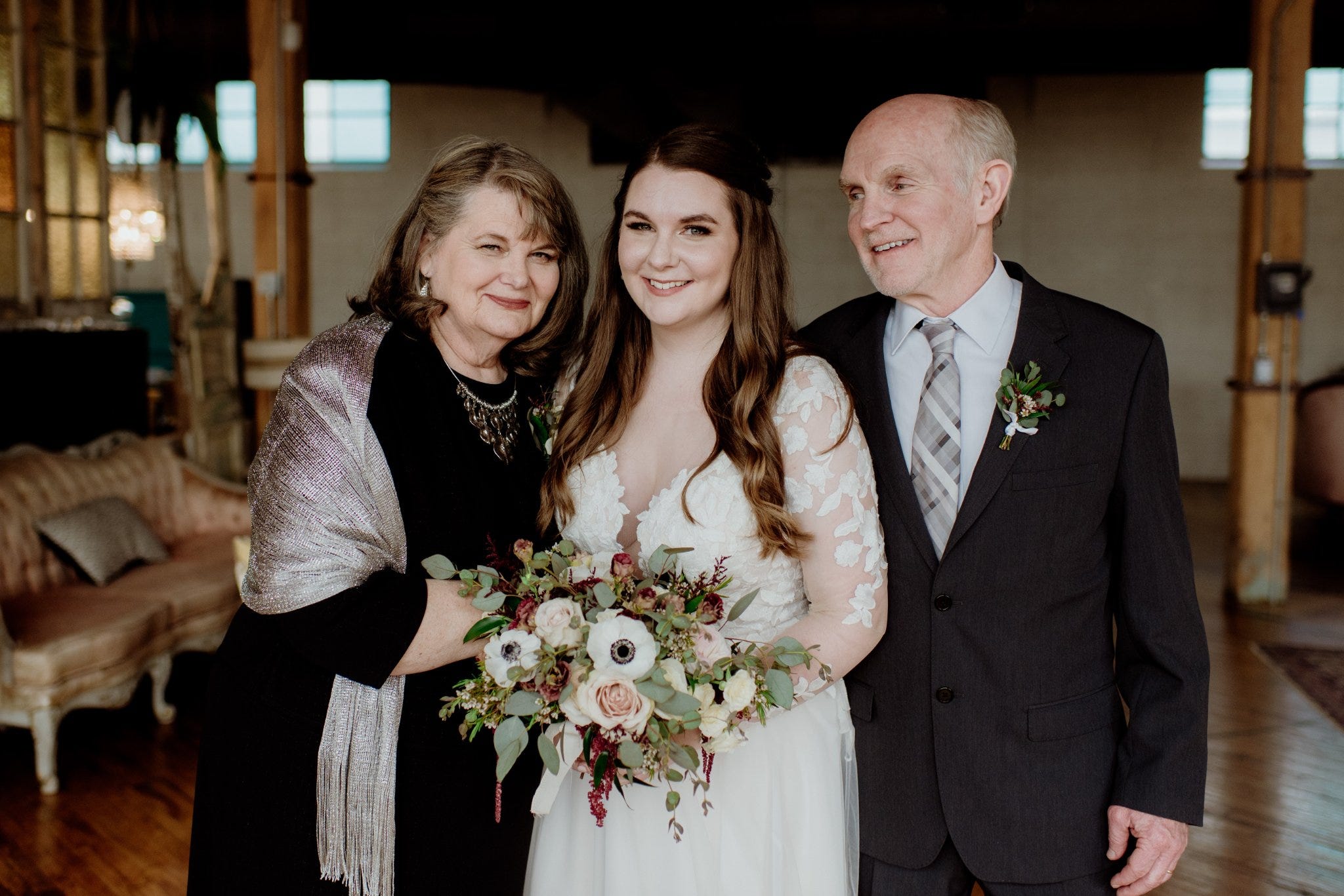 The author wearing a wedding dress and holding a bouquet standing between her parents on her wedding day.