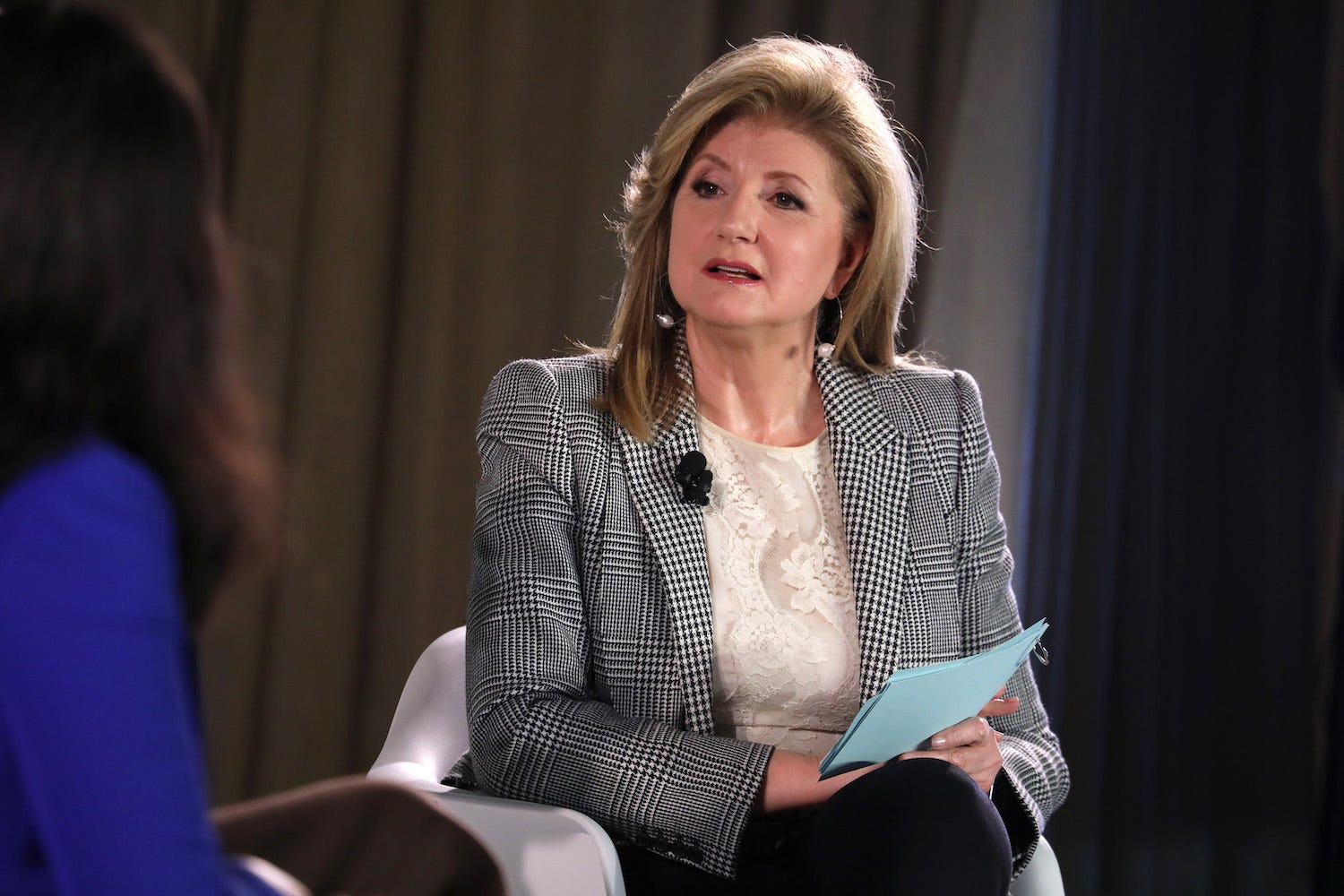 Arianna Huffington speaks onstage during the TIME 100 Health Summit at Pier 17 on October 17, 2019 in New York City. She's holding a blue card and wearing a grey jacket.