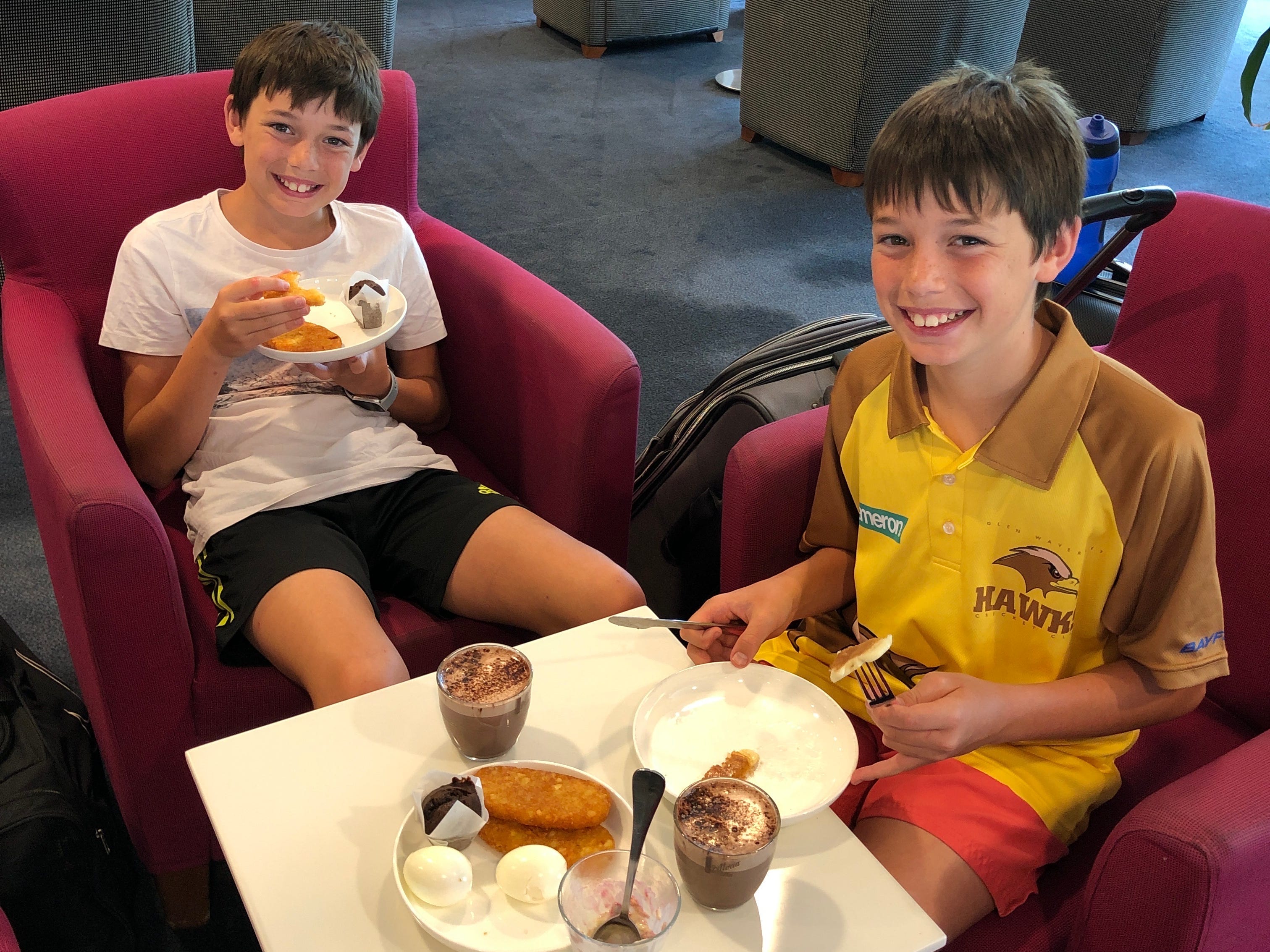Two young boys eat food in an airport lounge.