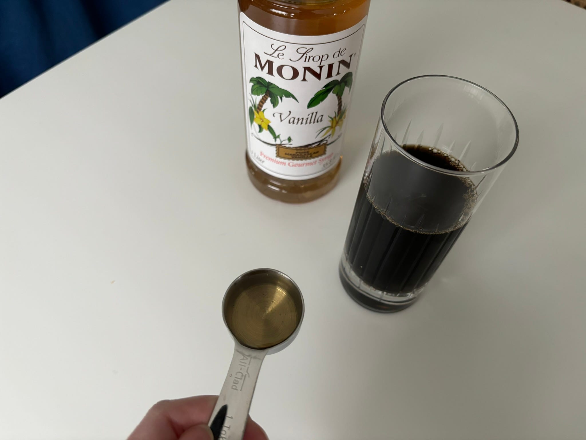 Spoonful of of vanilla syrup next to monin bottle and cup of coffee