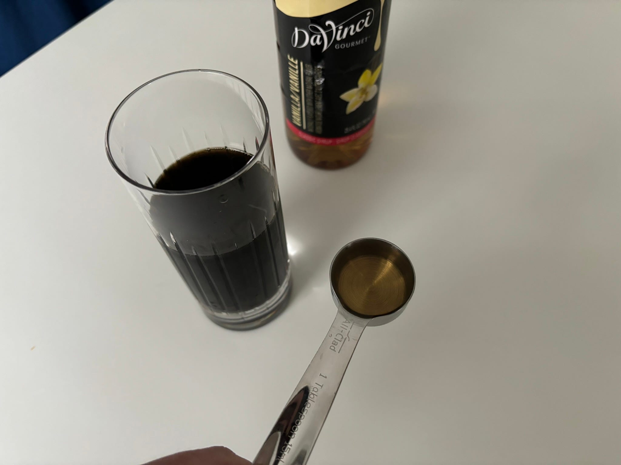Spoonful of of vanilla syrup next to DaVinci bottle and cup of coffee