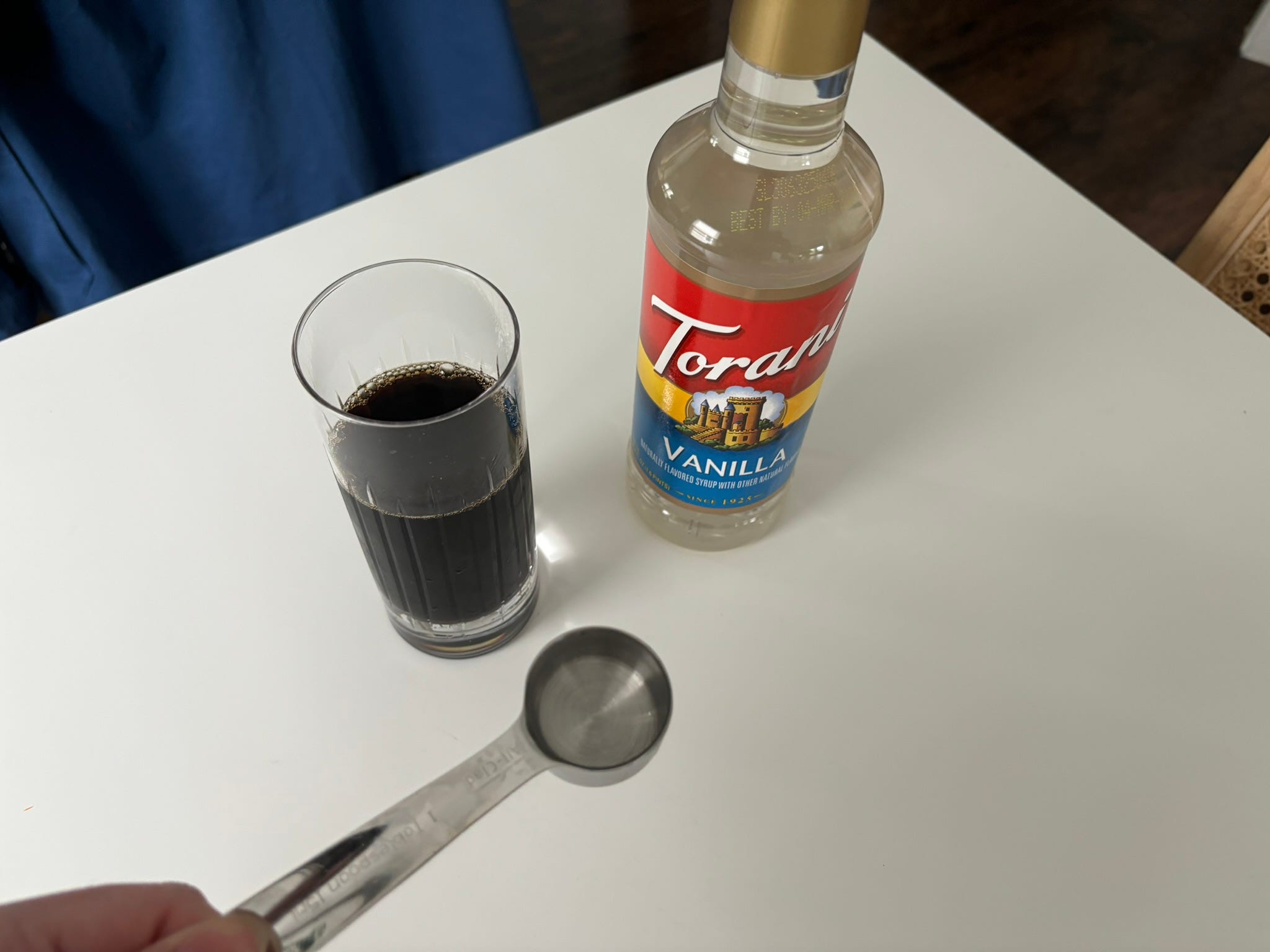 Spoonful of of vanilla syrup next to Torani bottle and cup of coffee