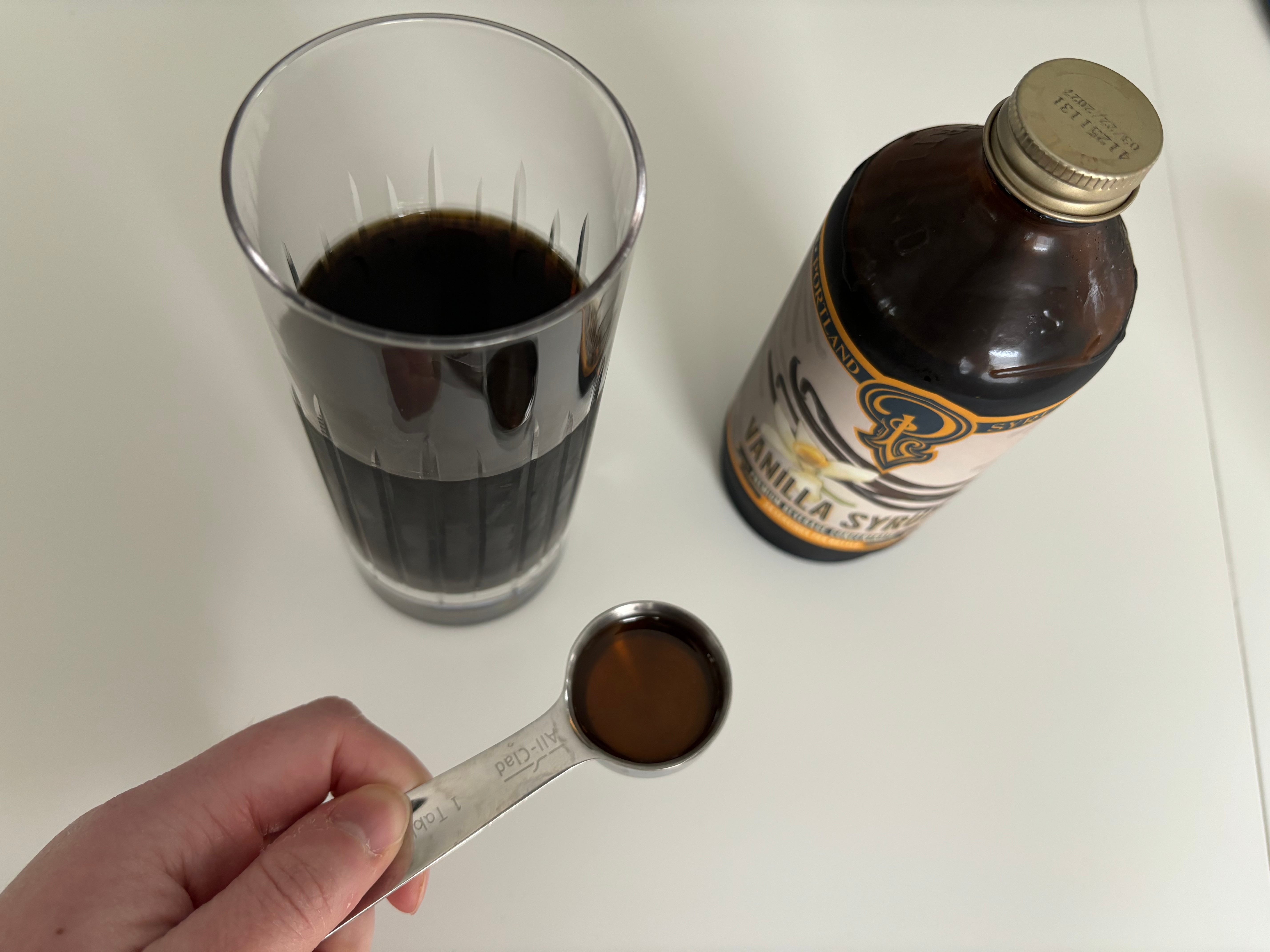 Spoonful of of vanilla syrup next to Portland Syrup bottle and cup of coffee