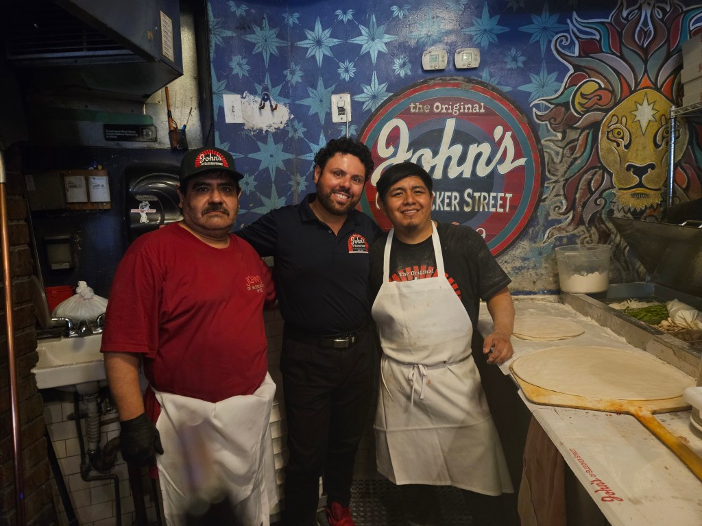 Three men posing in a pizza restaurant.