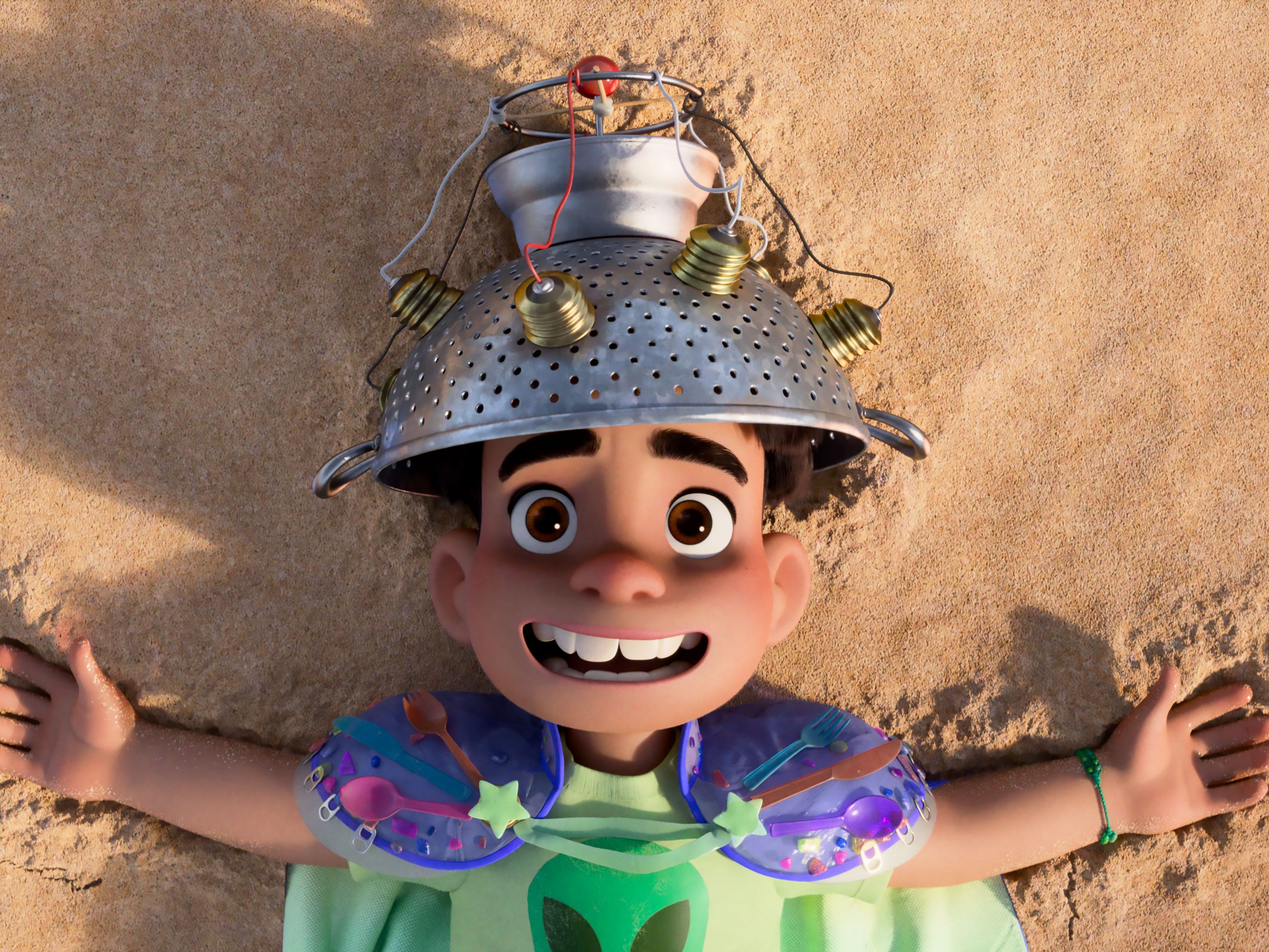 A still of "Elio" showing a kid lying down in sand with a metal helmet on his head.