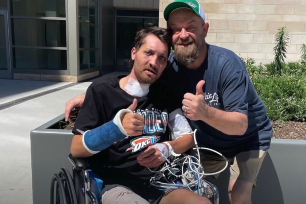 Injured man in wheelchair gives thumbs up with friend.