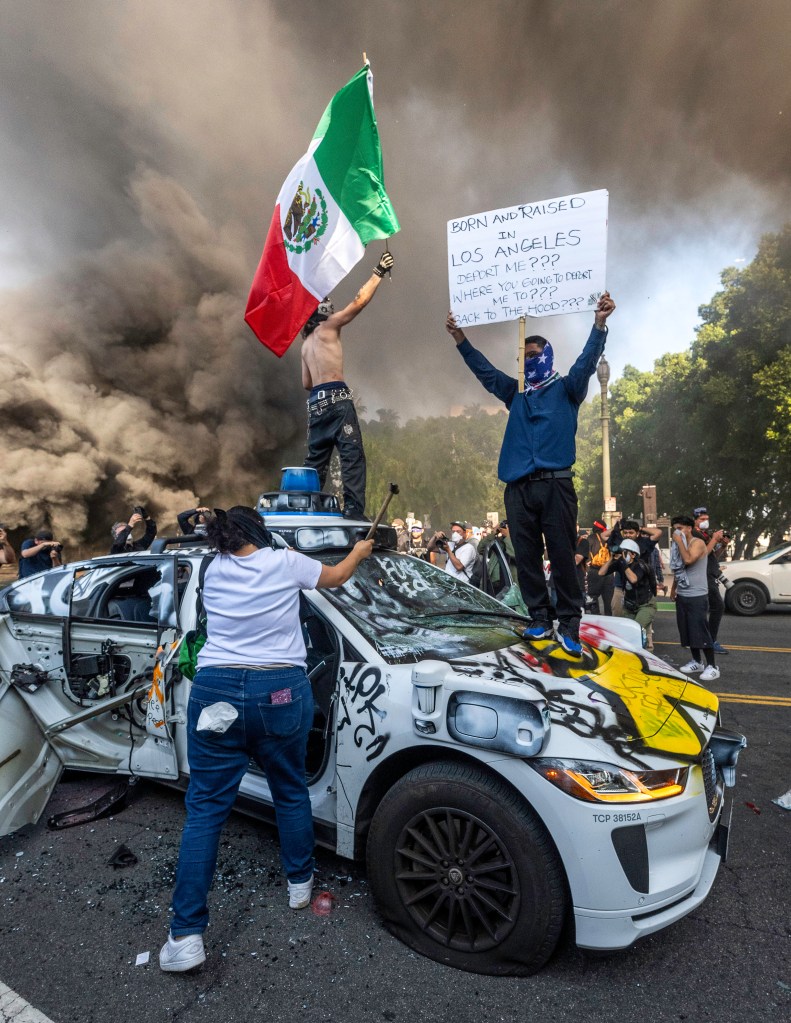 Protesters wave a Mexican flag on top of a destroyed car during the Los Angeles riots on June 8, 2025.