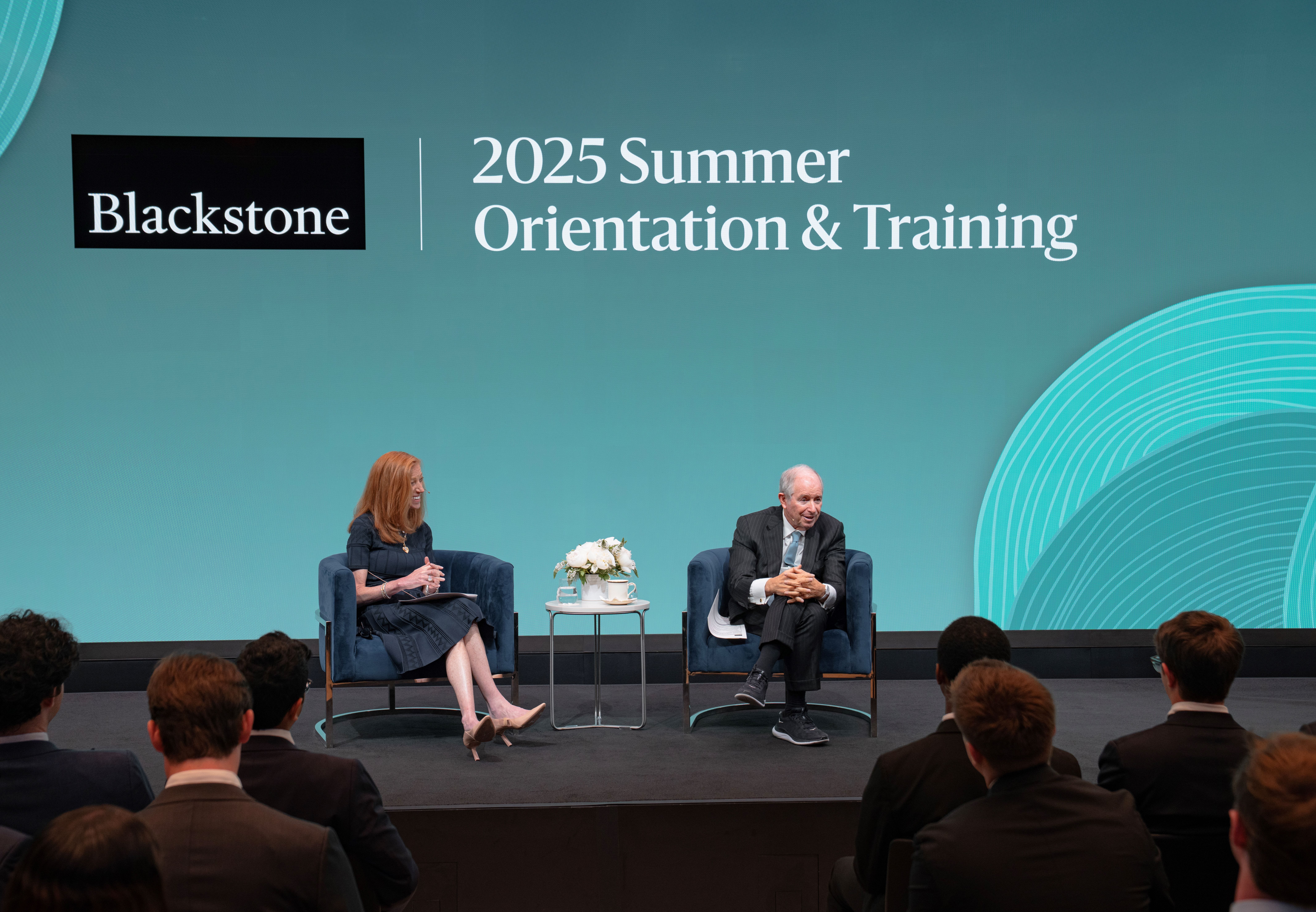 Paige Ross and Steve Schwarzman sit in front of a Blackstone-branded screen, while speaking to summer analysts.