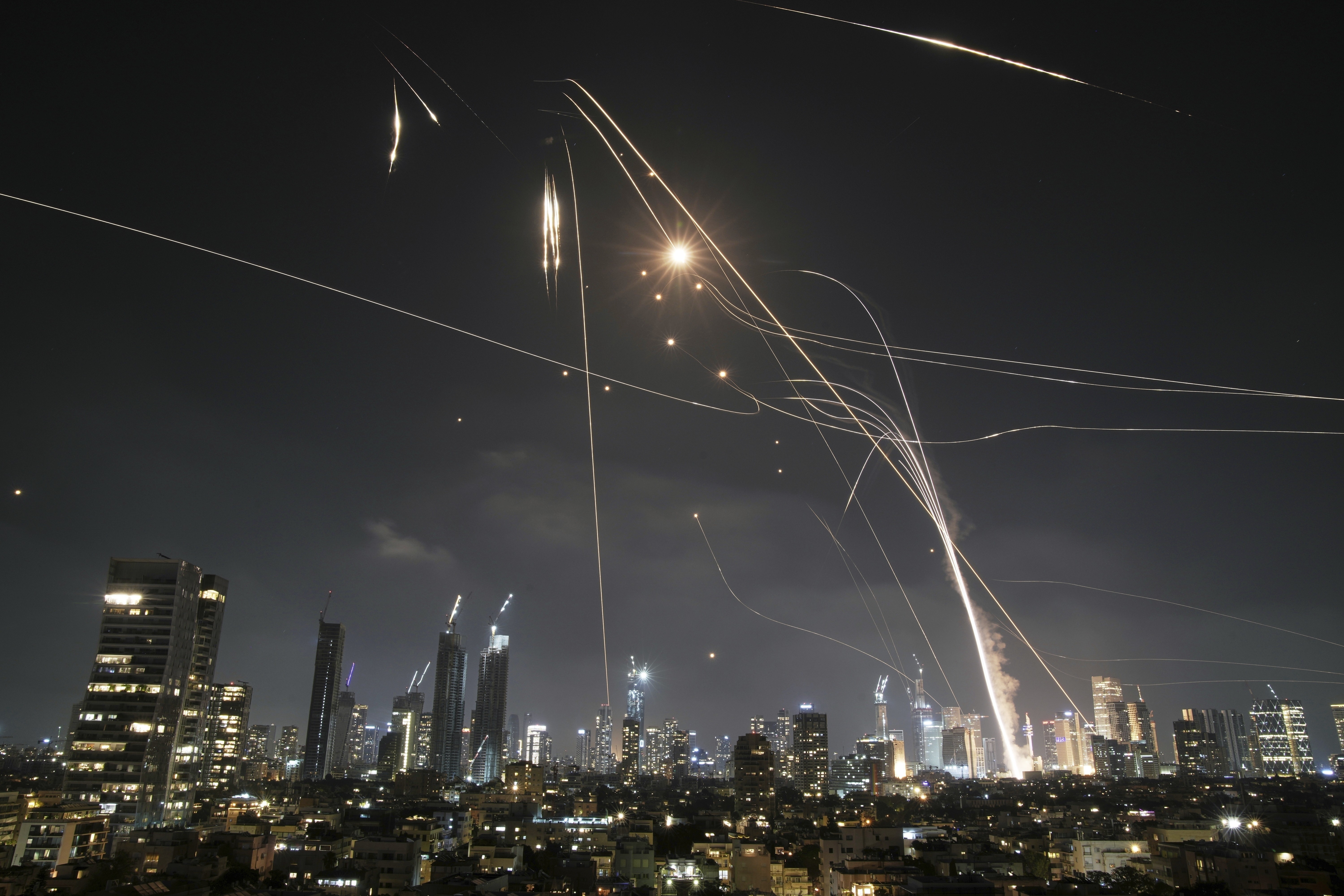 Light streaks are left in the sky above a city at night, as incoming missiles are met by defensive missiles.