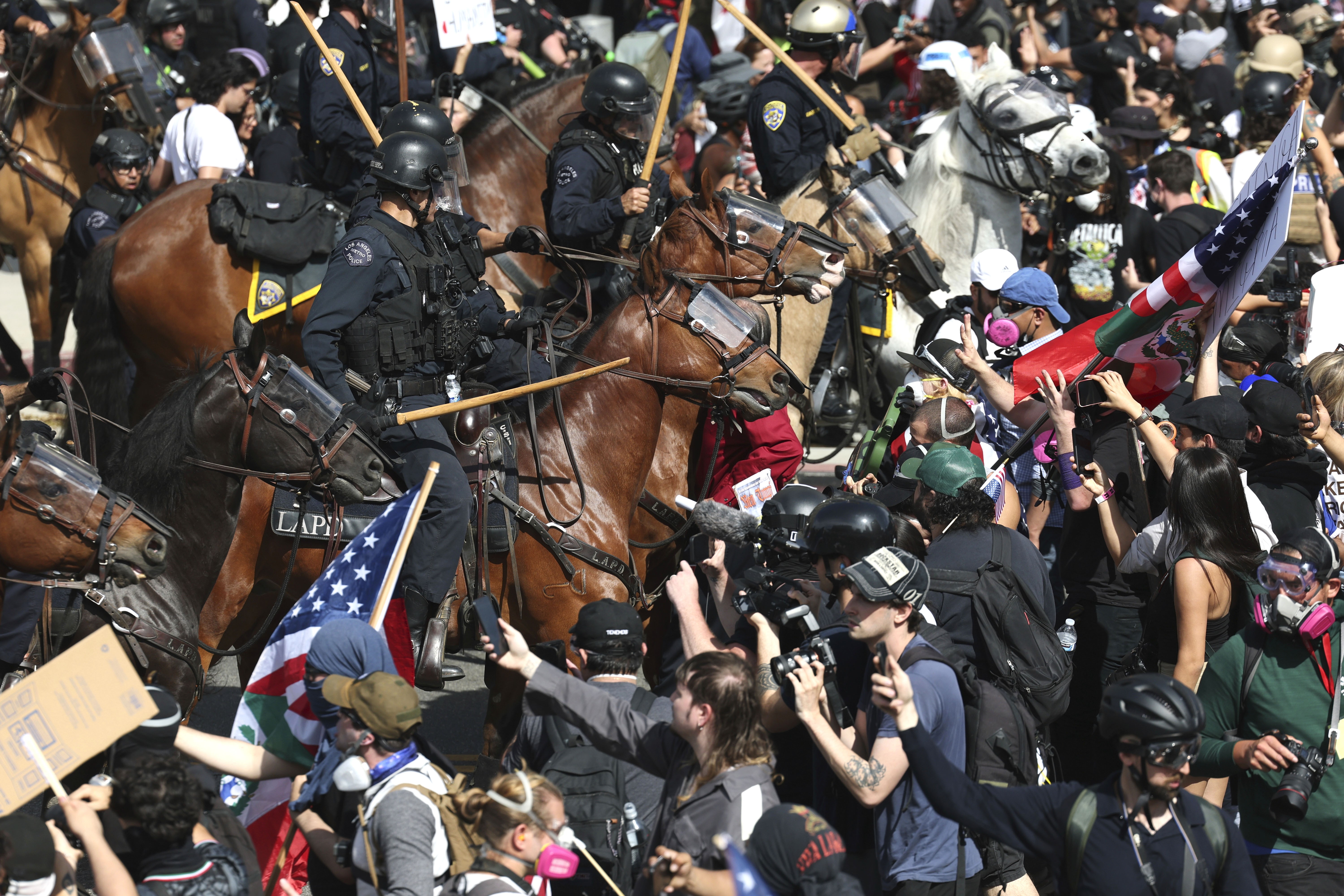 Riot police officers on horseback approach a large crowd of demonstrators.