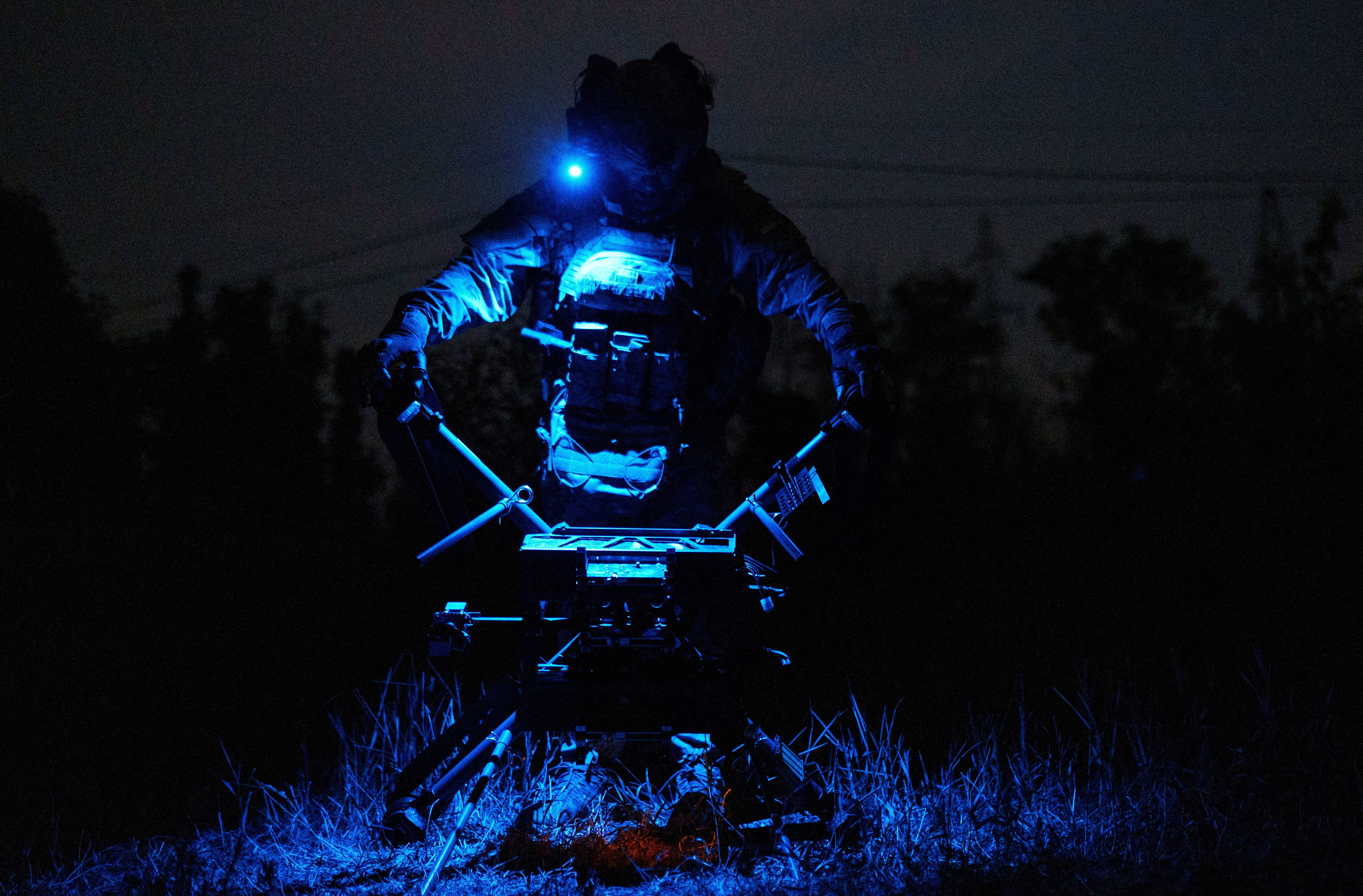 A soldier carries a large drone, seen at night.