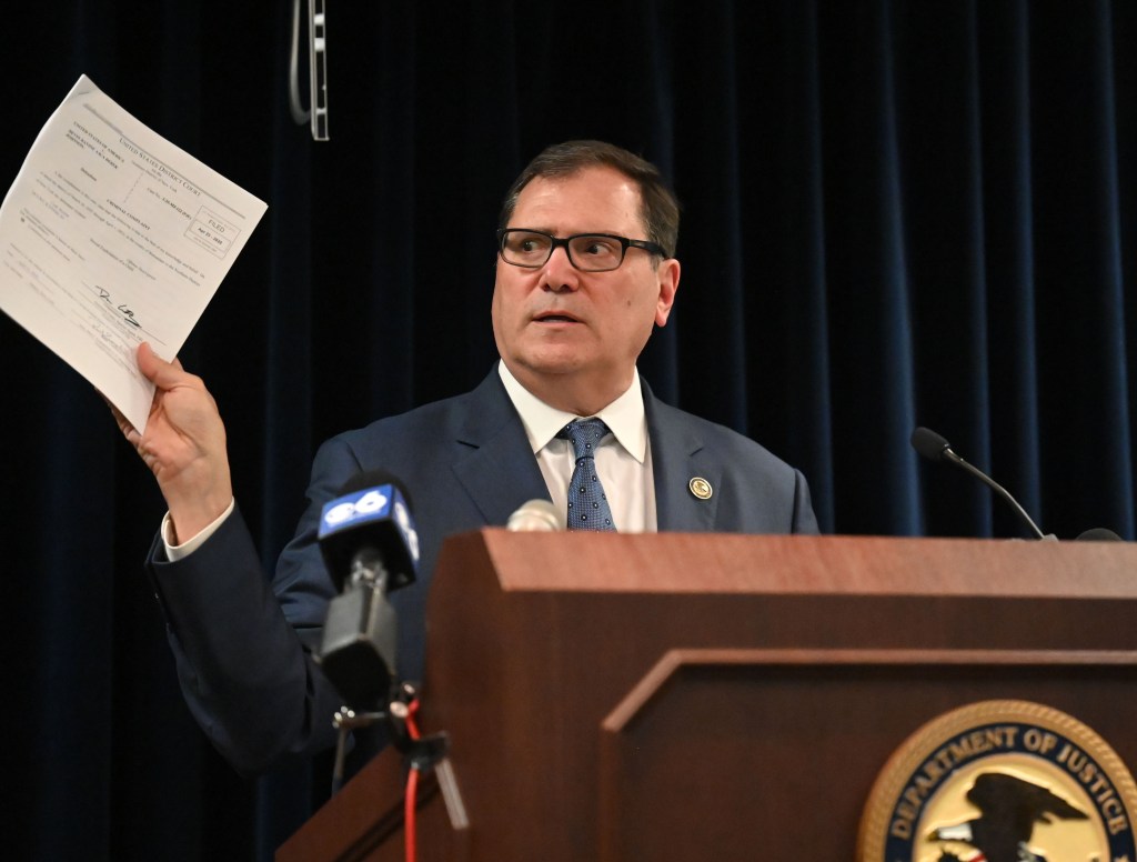 A U.S. Attorney holding a criminal complaint at a news conference.