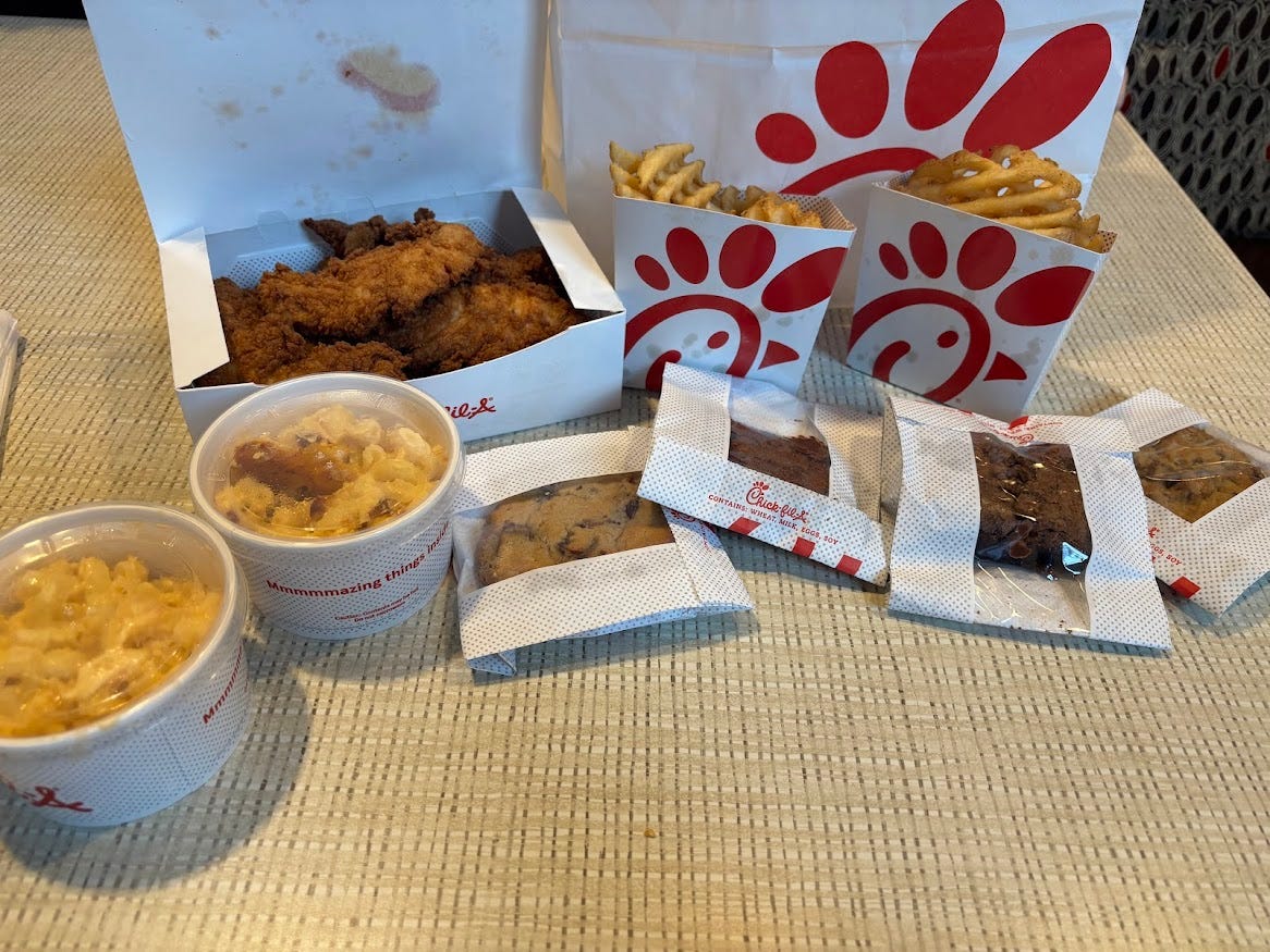 Chicken tenders, cookie, brownie, mac and cheese, waffle fries, laid out on table in front of Chick-fil-A bag