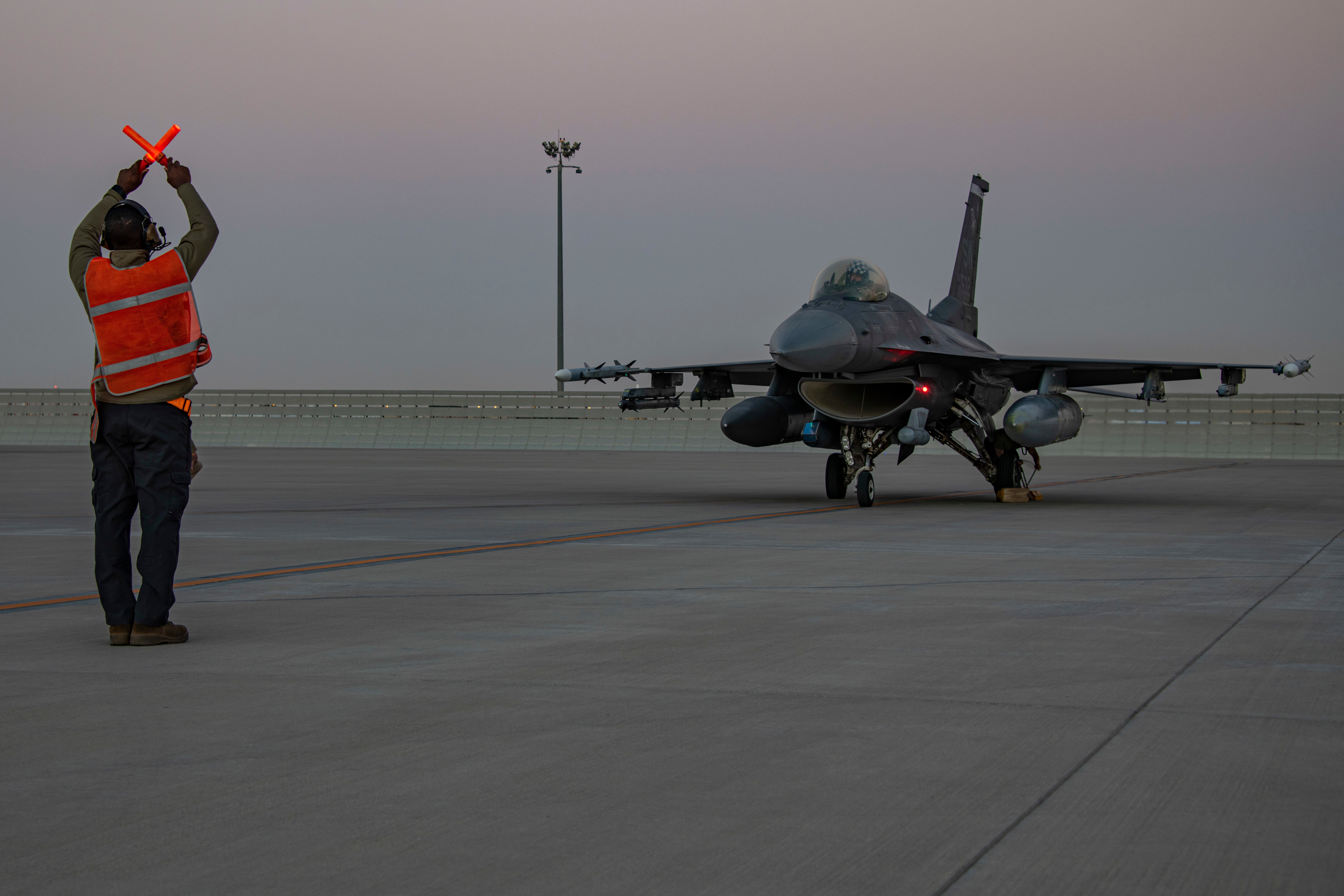 In this handout photo from the US Air Force, an airman guides an F-16 Fighting Falcon during training at Al-Udeid Air Base, Qatar, January 24, 2022.