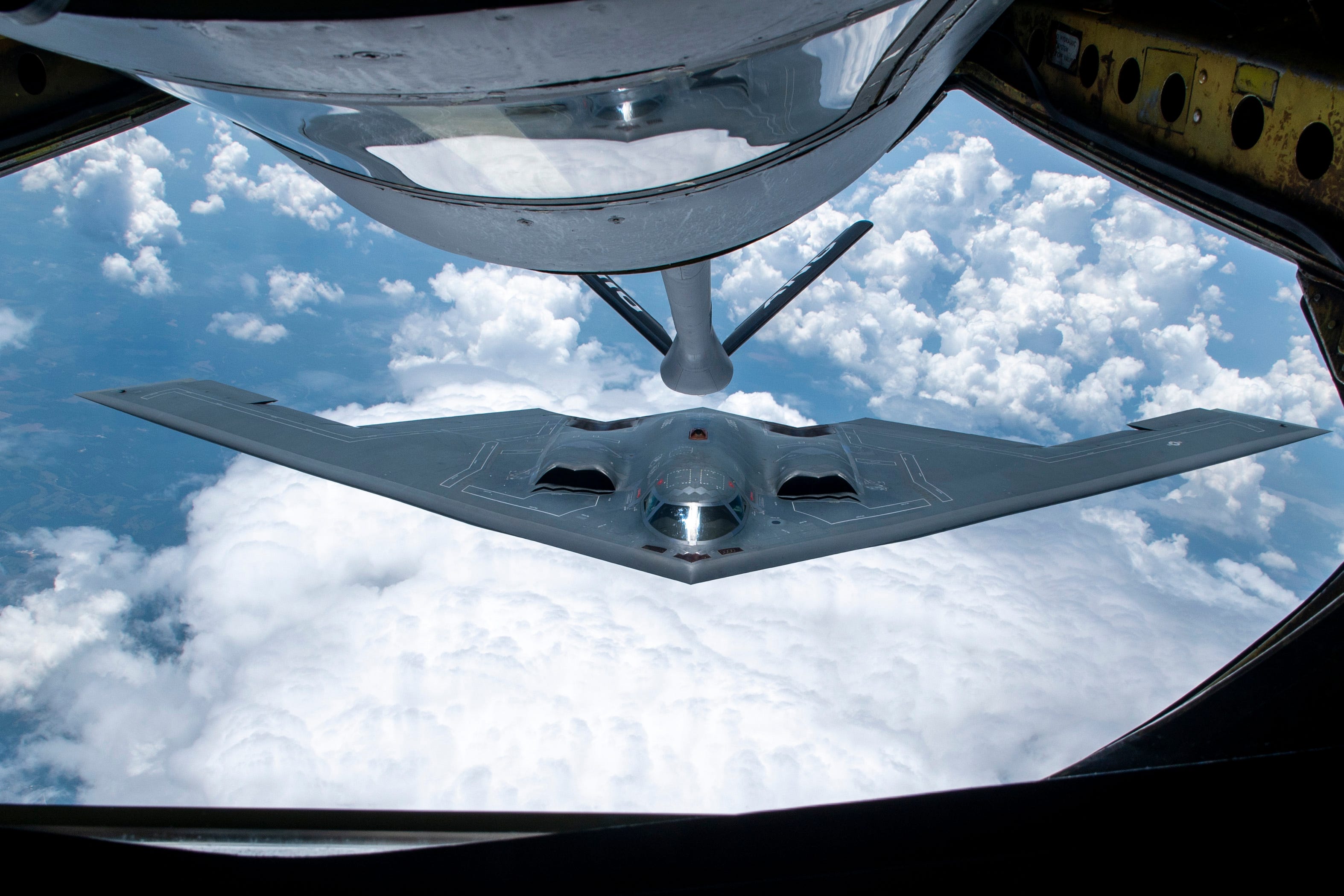 A B-2 Spirit flying above the clouds, viewed from a tanker aircraft during refueling.