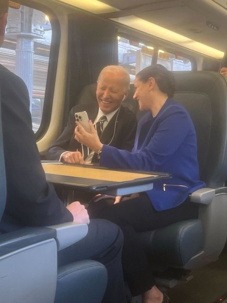 Joe Biden and a woman looking at a smartphone on a train.