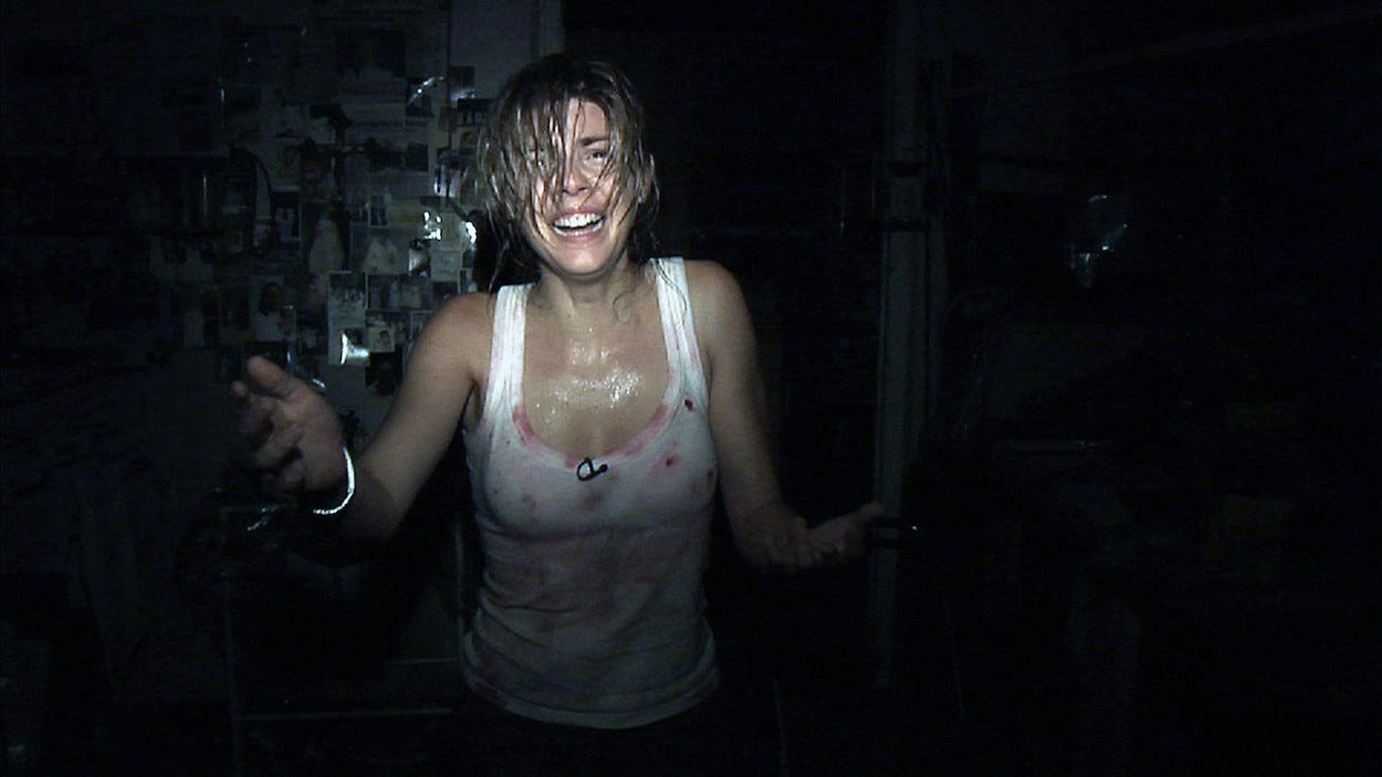 A woman in a white, bloody vest walks toward the camera.