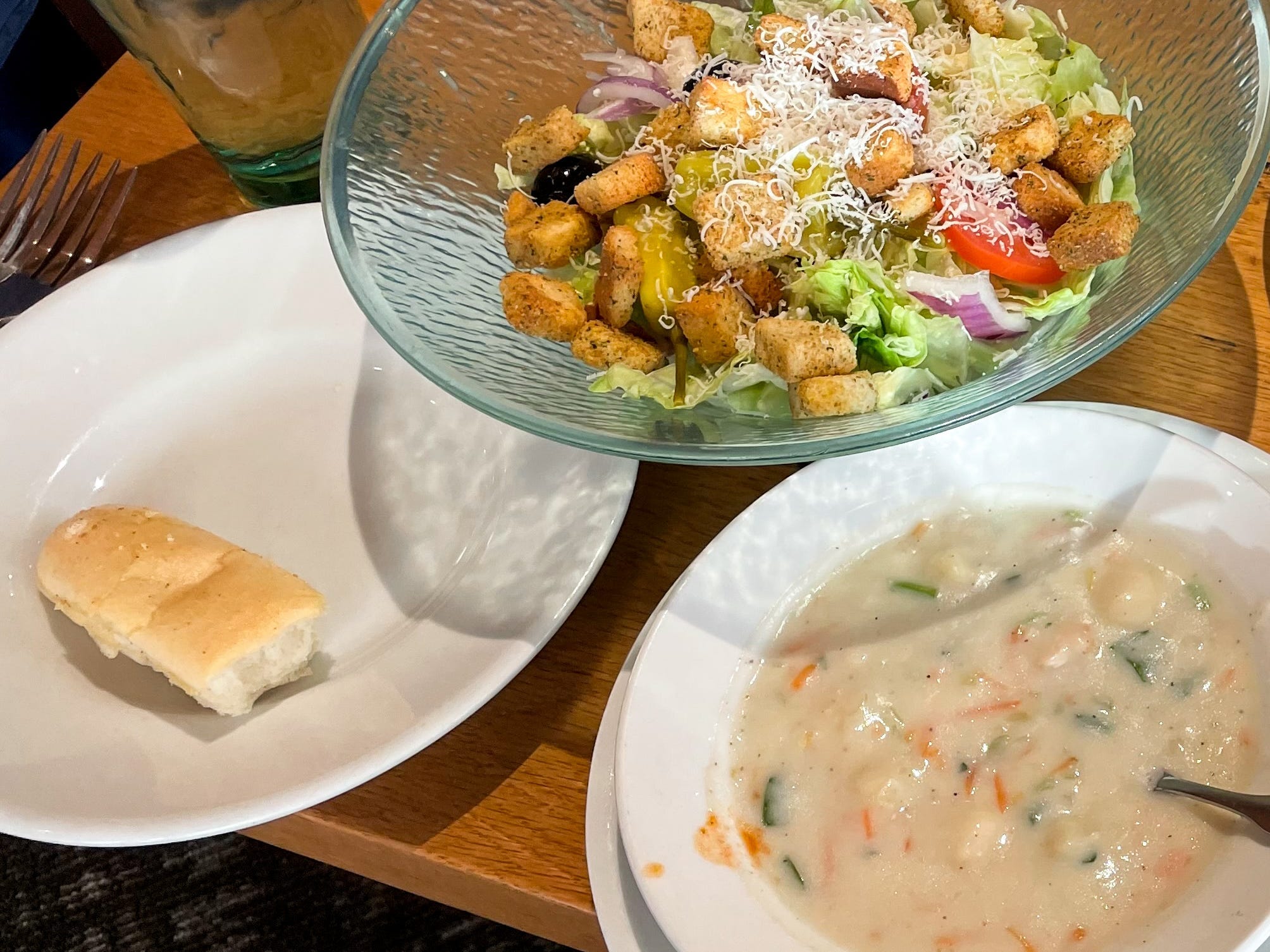 Four different pasta dishes, two different soups, a large bowl of salad, and a half-eaten breadstick on a table at Olive Garden.