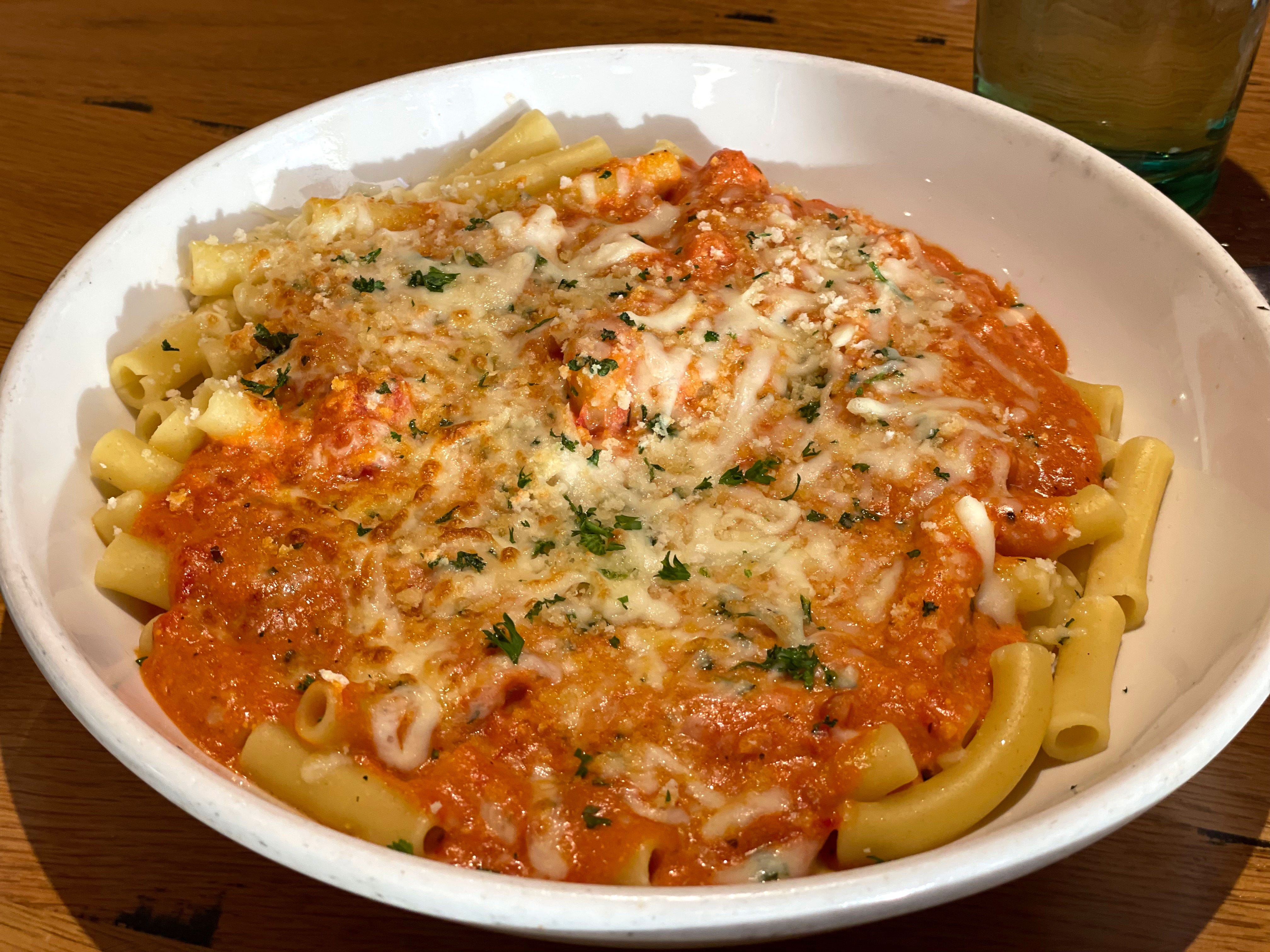 A bowl of ziti in pink sauce with melted cheese on top.