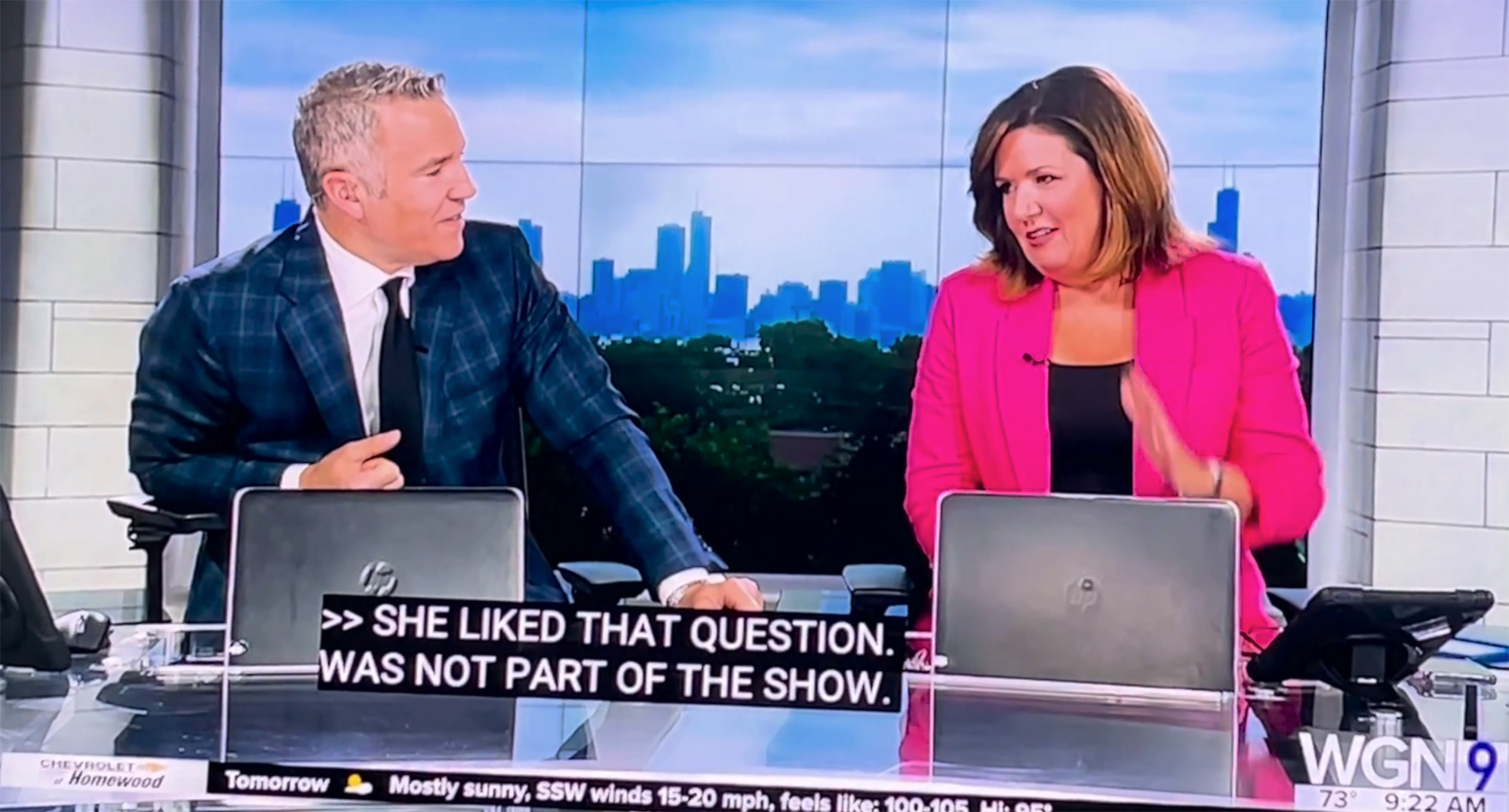 Two anchors sit at a desk on live TV. 