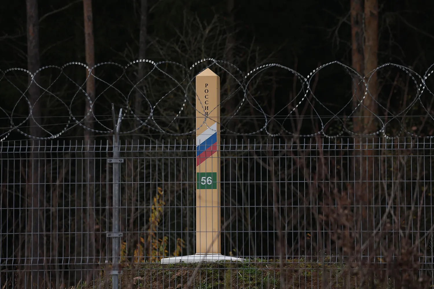 A pillar with a Russian flag on it seen behind a barbed wire topped fence.