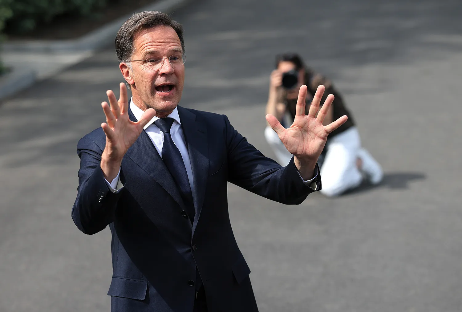 Mark Rutte waves both hands as he speaks. A photographer kneels on the ground behind him to take a photo.