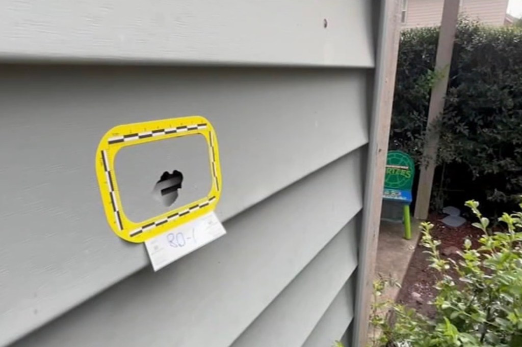 Bullet hole in house siding marked with evidence scale.