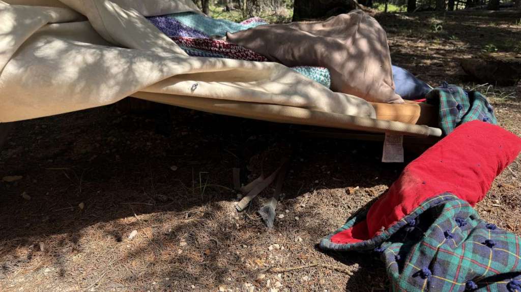 Camp cot under a tarp with blankets and pillows.