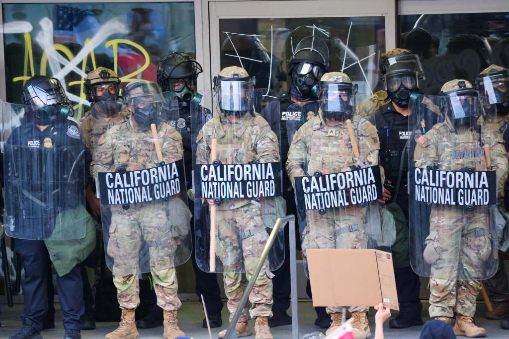 California National Guard members in riot gear face anti-ICE protestors.