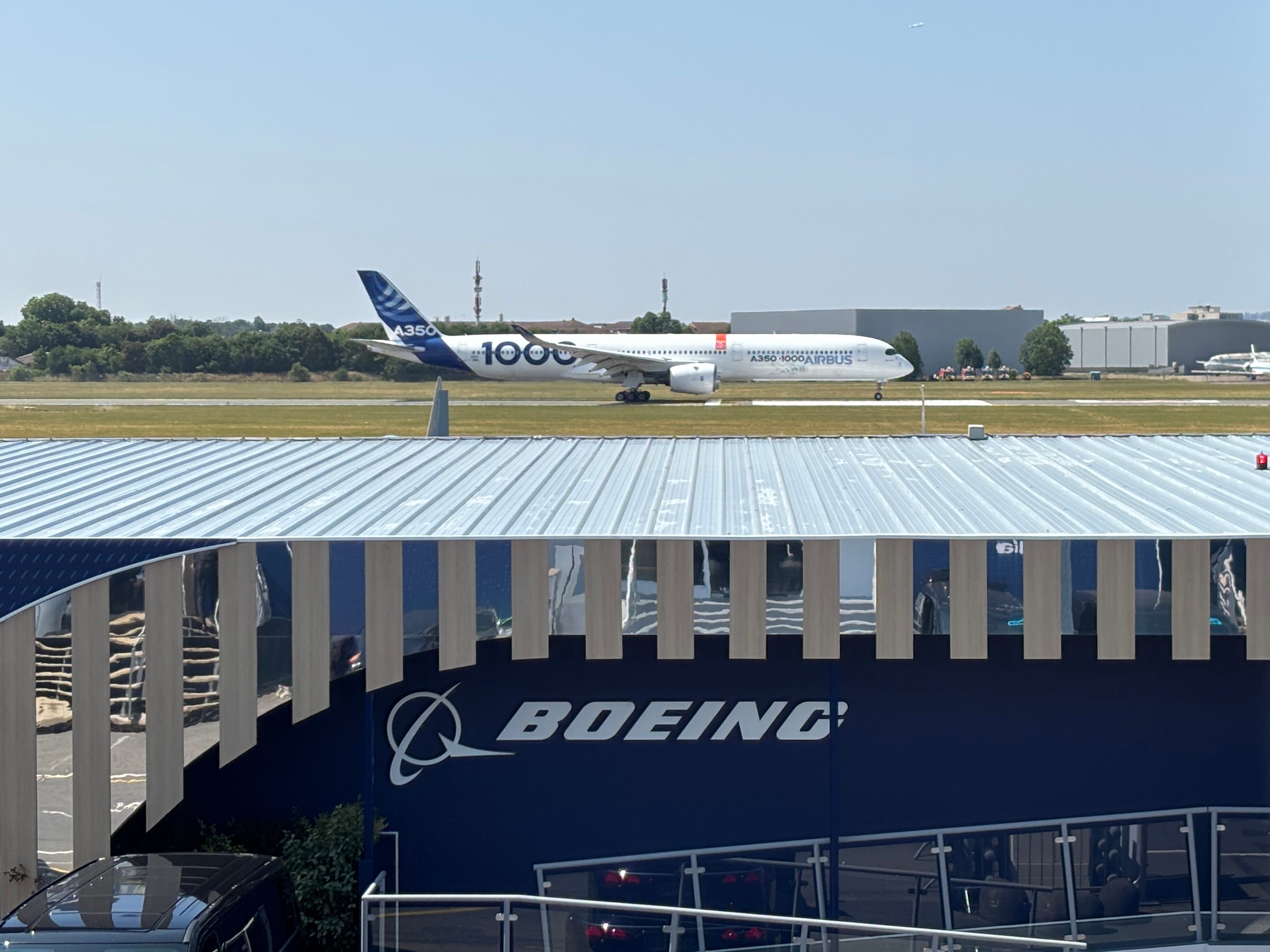 An Airbus A350-1000 takes off on the runway at Le Bourget Airport, behind a Boeing Chalet at the 2025 Paris Air Show