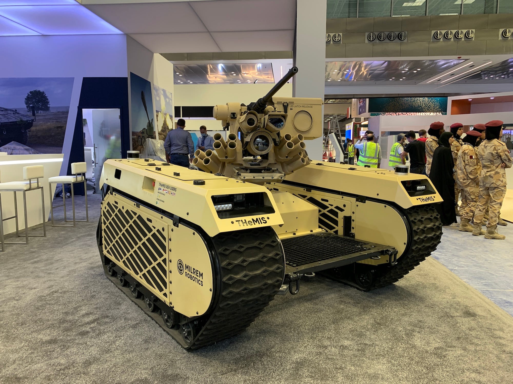 A yellow coloured large robot with tracks and a turret on display in a conference room