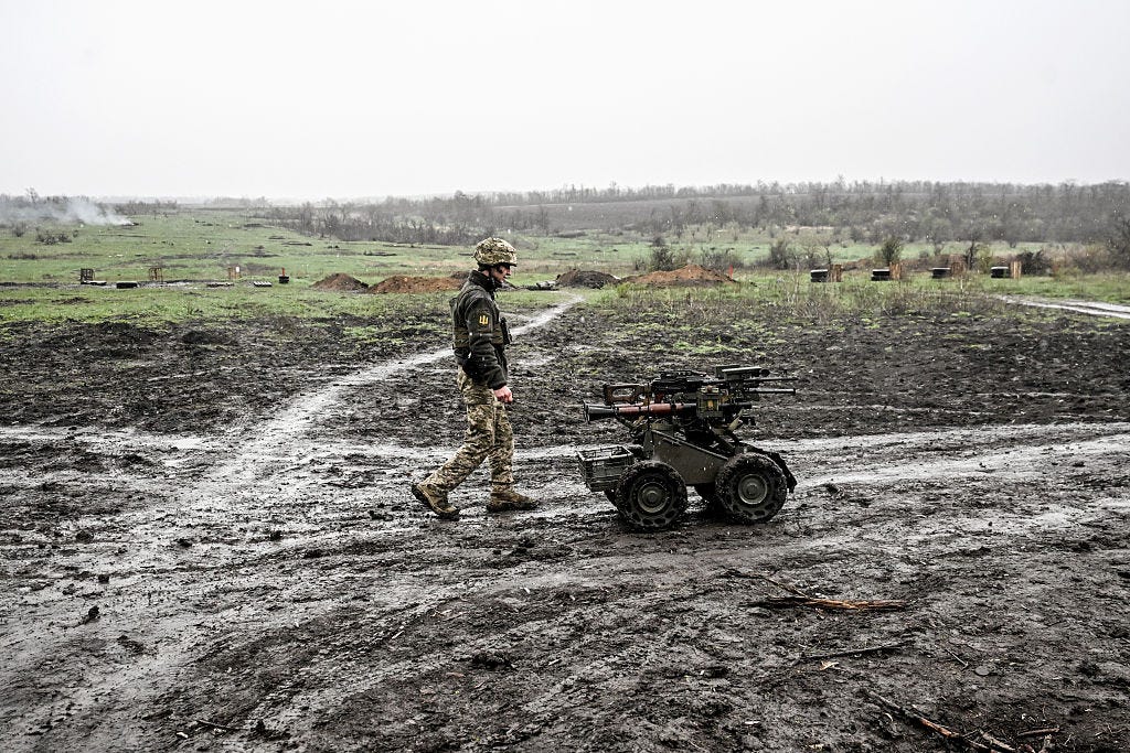 A soldier walks through a muddy field with an uncrewed ground robot.