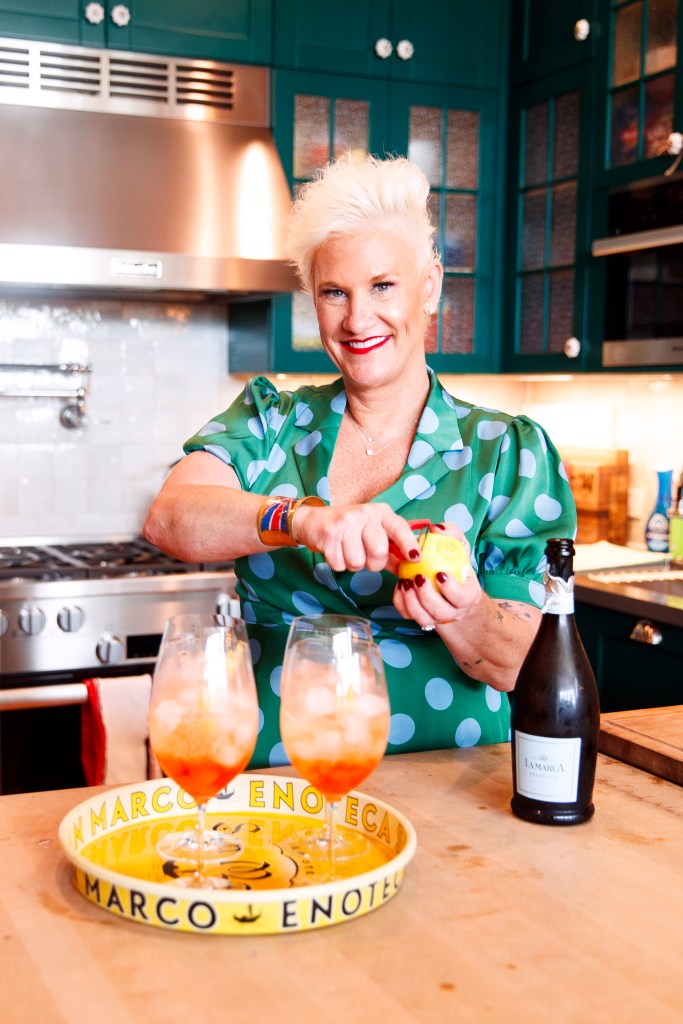 Anne Burrel with a bottle of proscecco slicing an orange.
