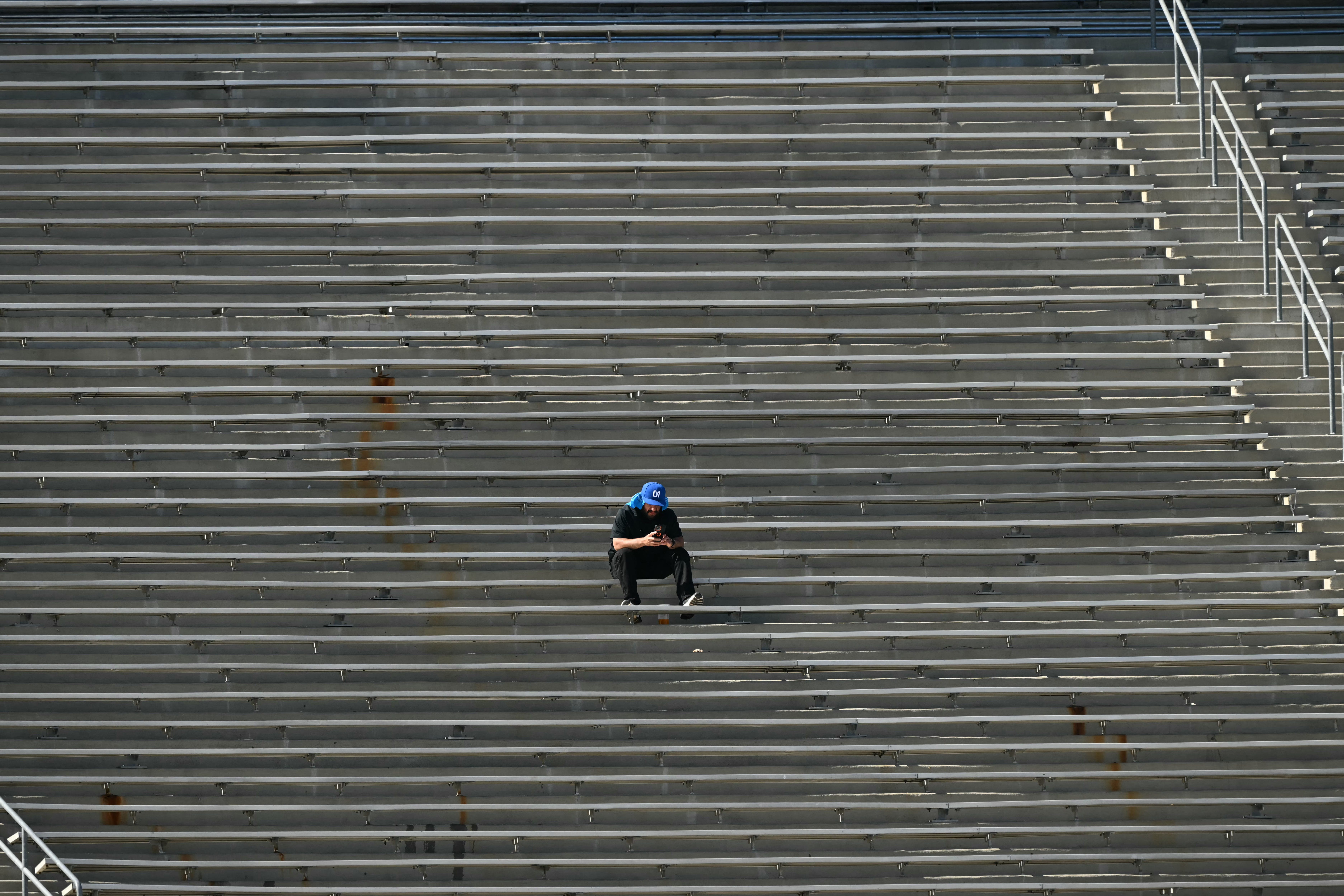 A fan watches his phone as he waits amid empty benches ahead of the FIFA Club World Cup 2025 Group E football match between Mexico's Monterrey and Italy's Inter Milan at the Rose Bowl stadium in Pasadena on June 17, 2025.