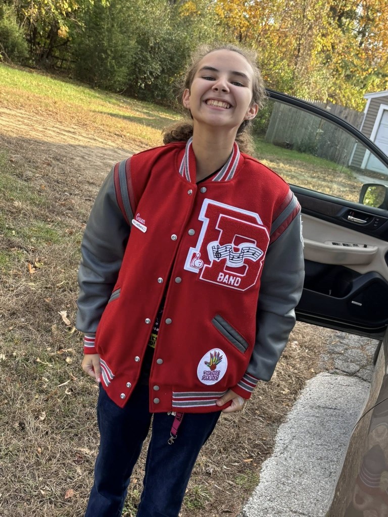 Girl smiling in red and gray letterman jacket. standing out side next to an open car door
