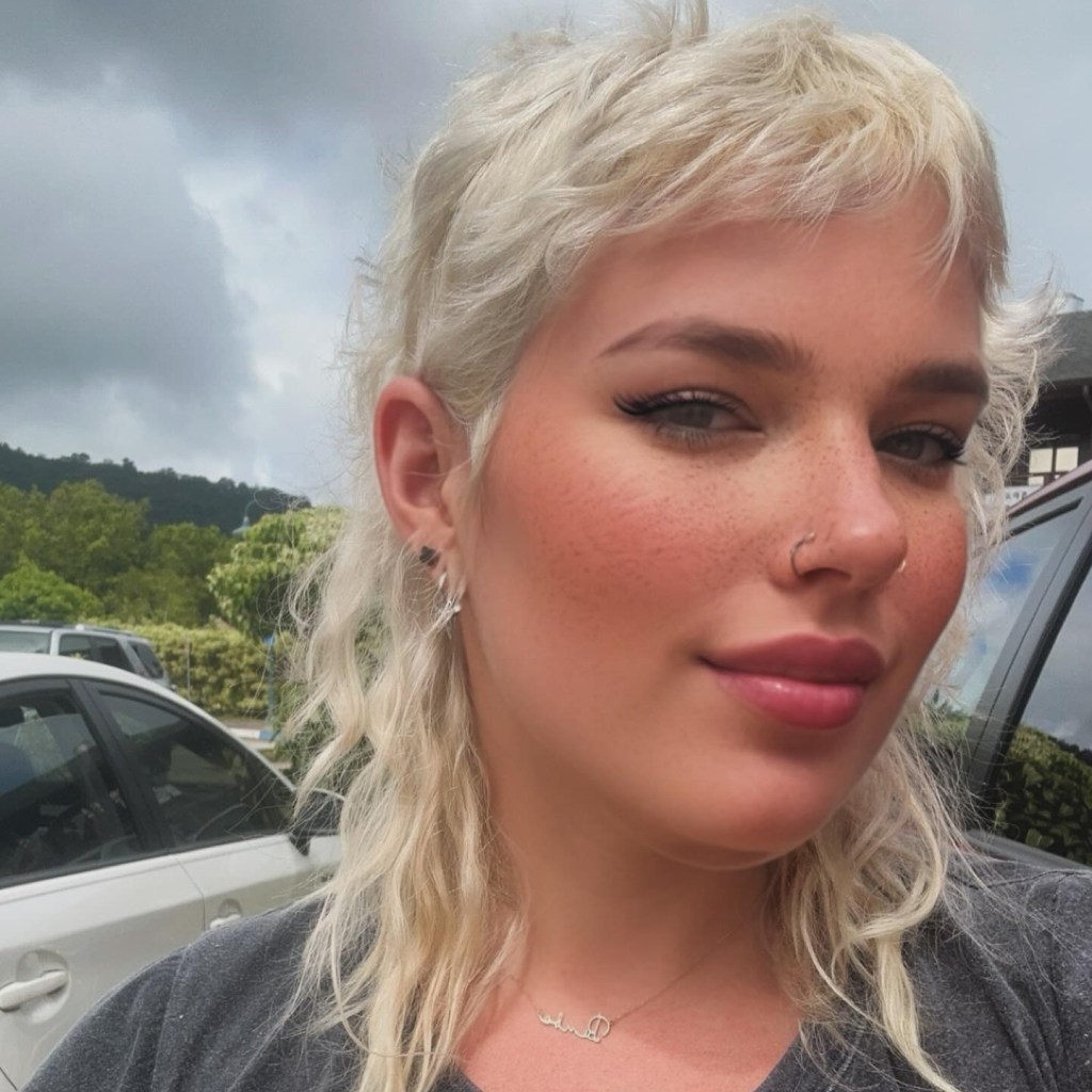 Woman with blonde, wavy mullet hairstyle and nose ring.