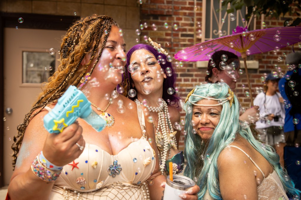 Three women in mermaid costumes at the Coney Island Mermaid Parade blowing bubbles.