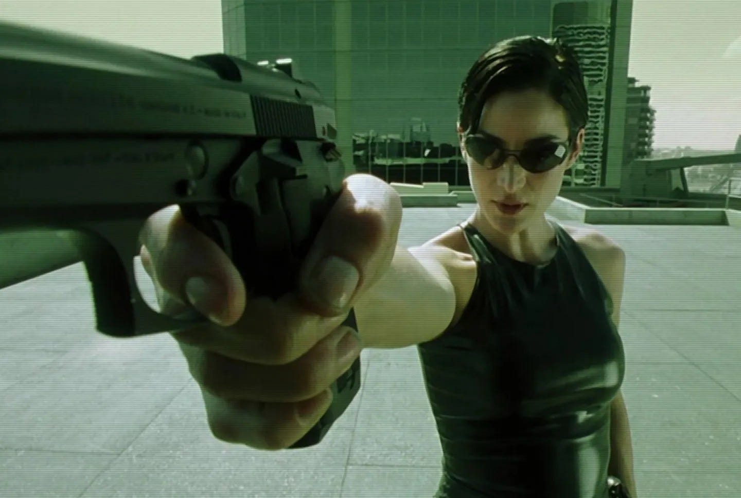 Carrie-Anne Moss holding a gun and wearing sunglasses
