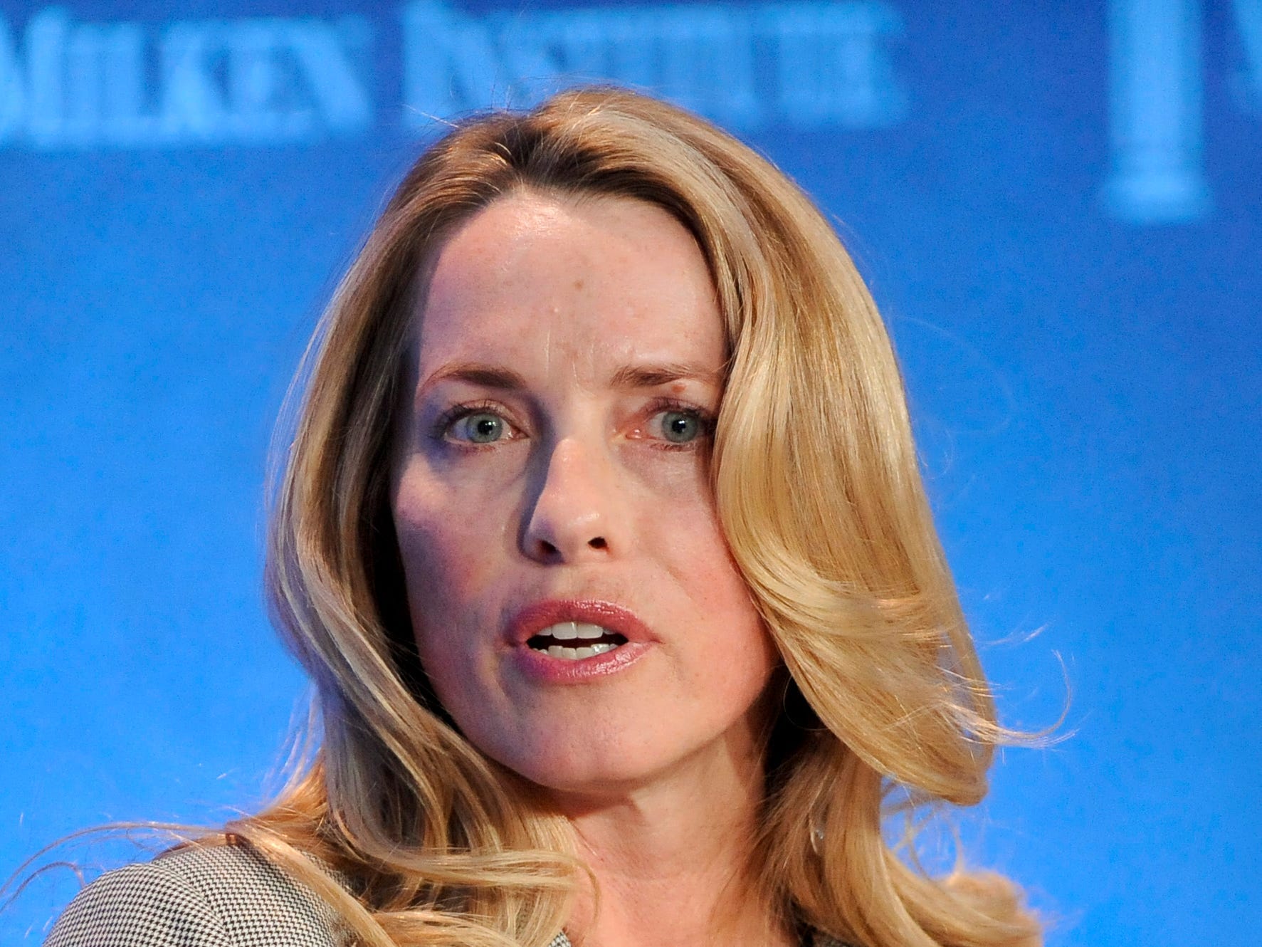 Laurene Powell Jobs dressed in a grey suit and talking on a stage, waves her hand forward to make a point