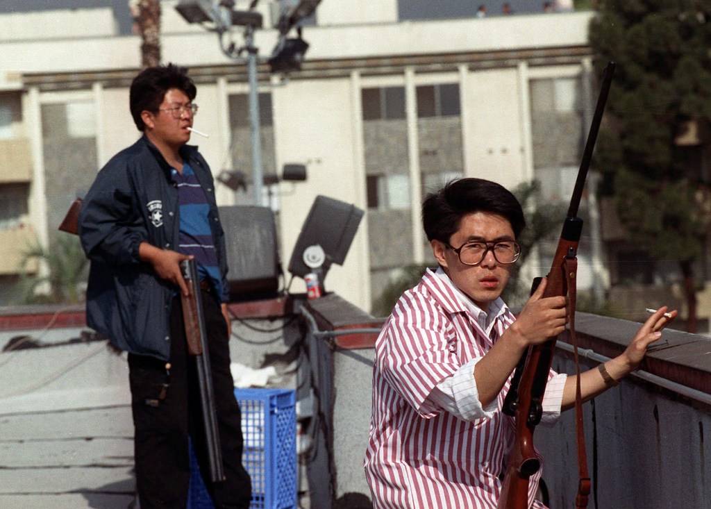 Two Korean men guard a rooftop with rifles during the 1992 Los Angeles riots.