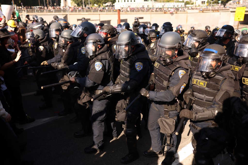 Riot police in full gear facing a crowd of protestors in 2025.
