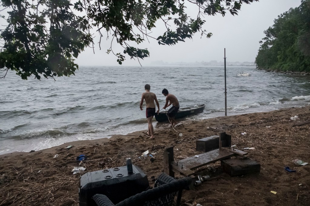 Two shirtless men pull a canoe onto a beach littered with debris.