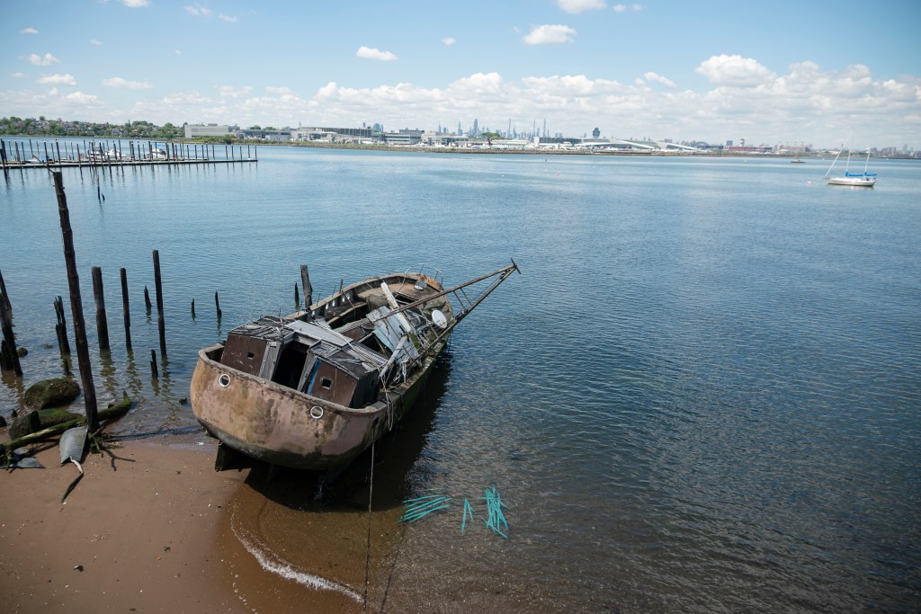 Wrecked boat on a shore with a city skyline in the background.
