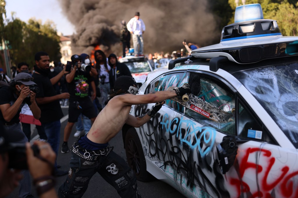 A person smashing a car window with a skateboard during a protest.